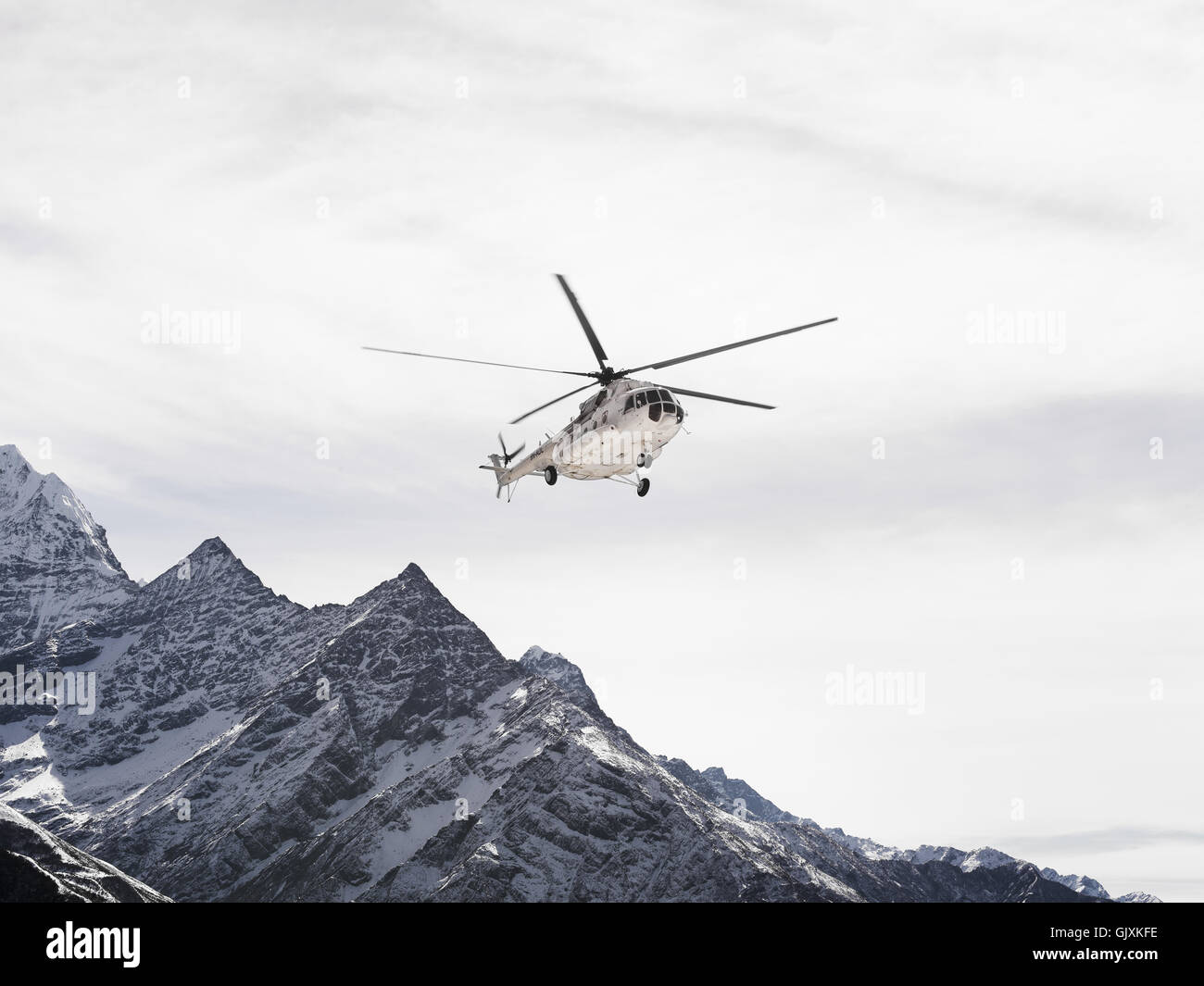 A helicopter flies over the jagged, snow covered mountains of Nepal's Everest Base Camp Stock Photo