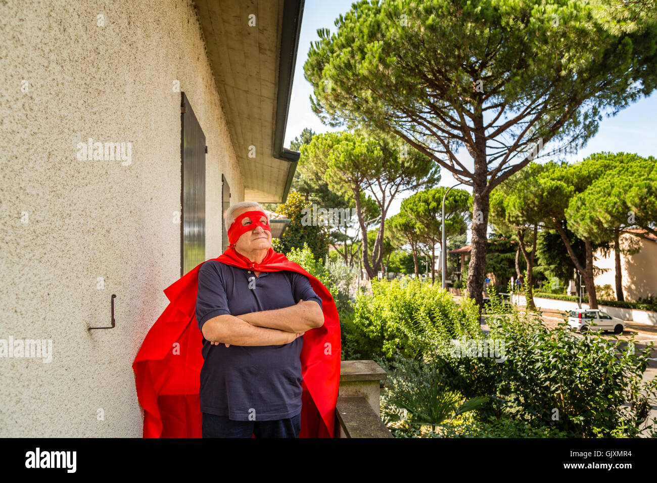 Funny and smiling senior man dressed as superhero with red cape and ...