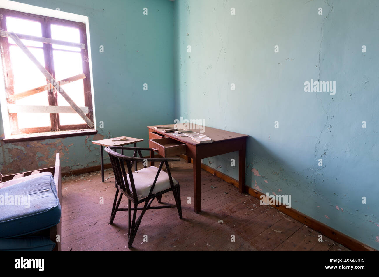 Interior of a dirty empty deserted room with office desk chair and bed Stock Photo