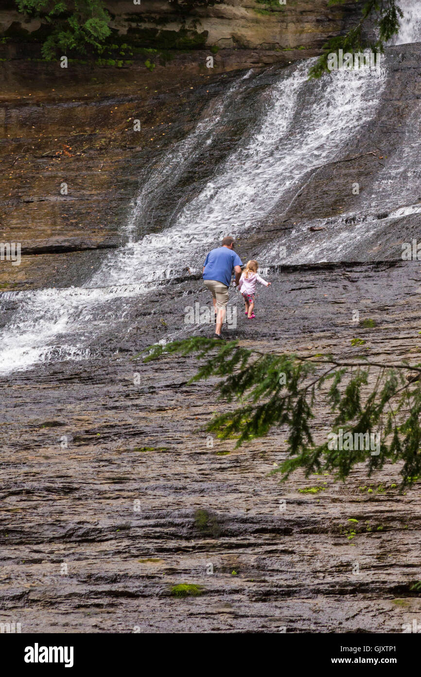 Sundell, Michigan - A man climbs with a small child over wet rocks adjacent to Laughing Whitefish Falls. Stock Photo