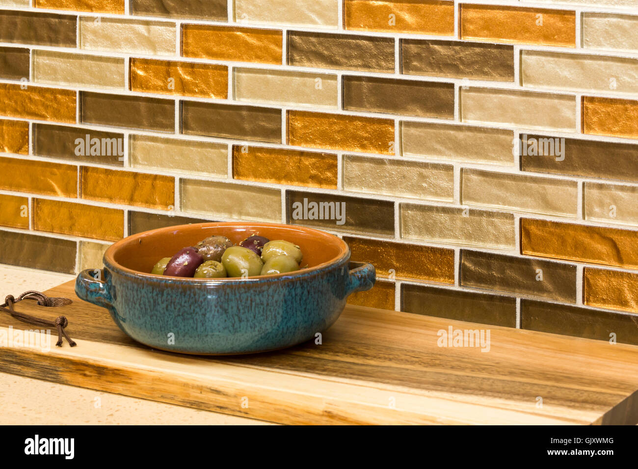 Home kitchen interior detail. Olives appetizers in ceramic serving dish on countertop with glass mosaic tile backsplash. Stock Photo