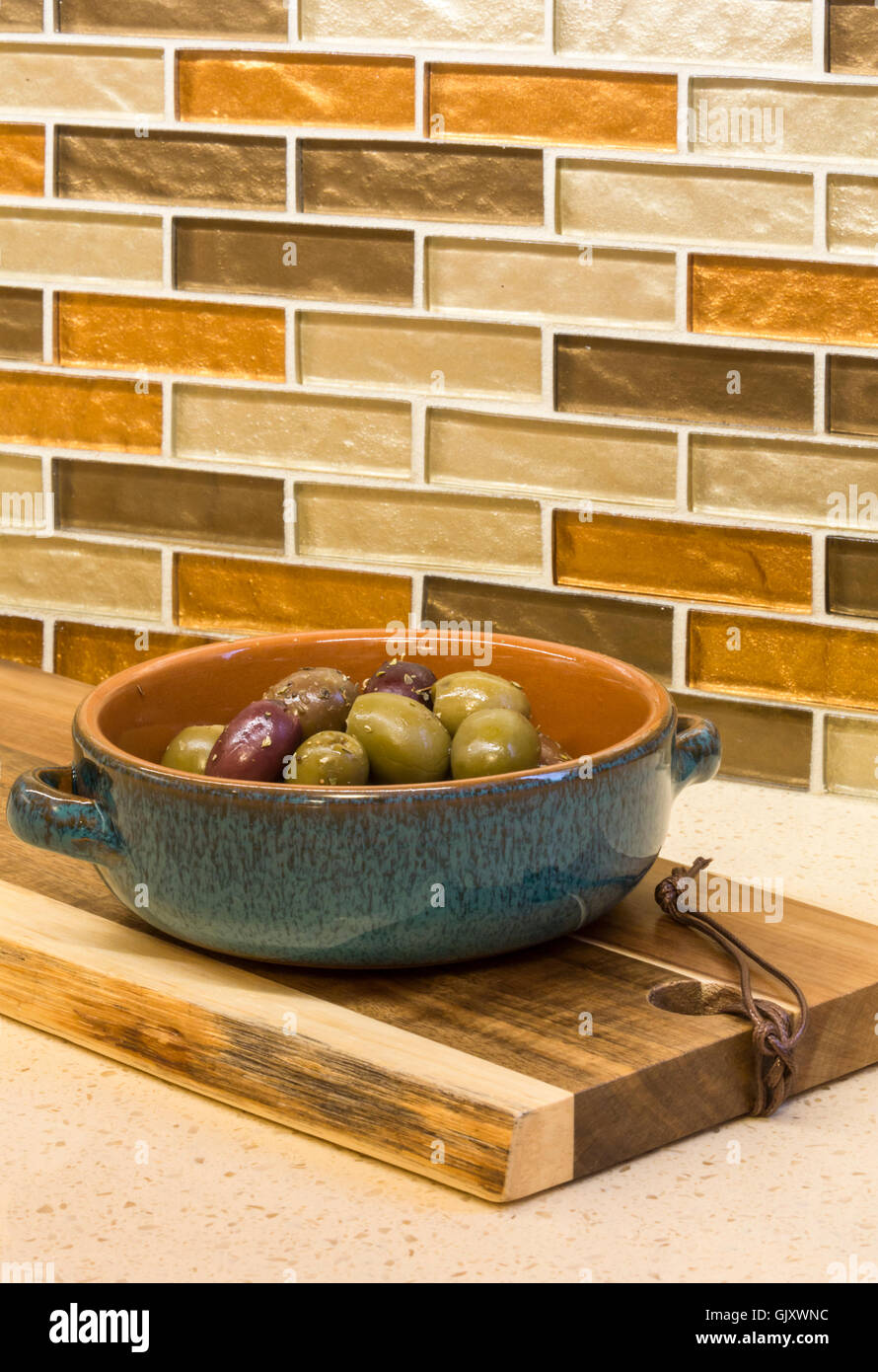 Home kitchen interior detail. Olives appetizers in ceramic serving dish on countertop with glass mosaic tile backsplash. Stock Photo