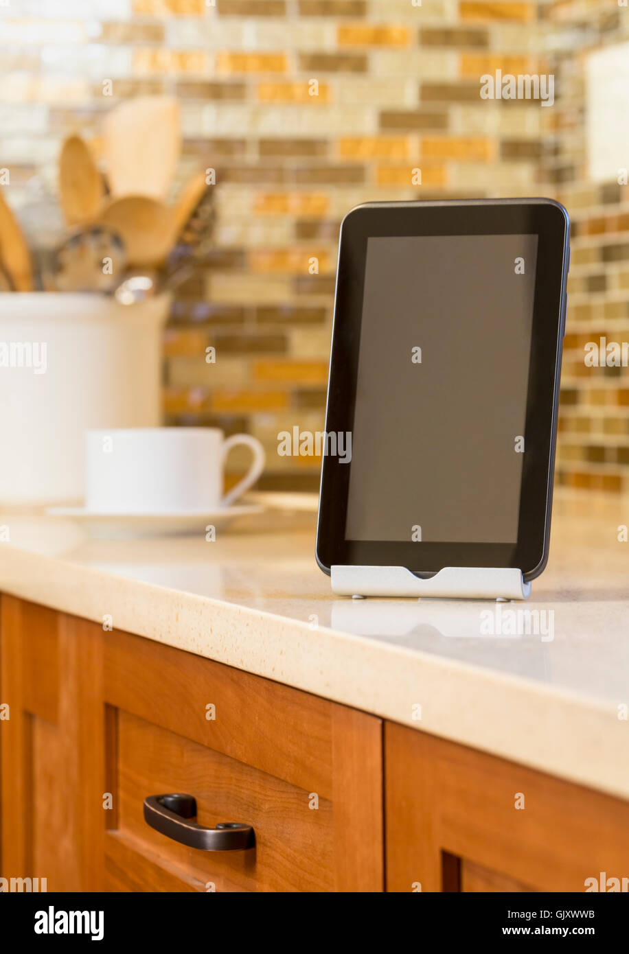 Close-up of tablet computer tech devices on quartz countertop in contemporary home kitchen. Selective focus on tablet with blank screen display. Stock Photo