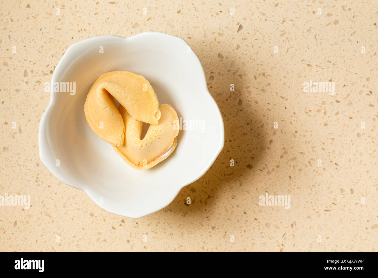 Two Chinese fortune cookies in a white ceramic bowl on a quartz engineered stone countertop in contemporary upscale home kitchen interior Stock Photo