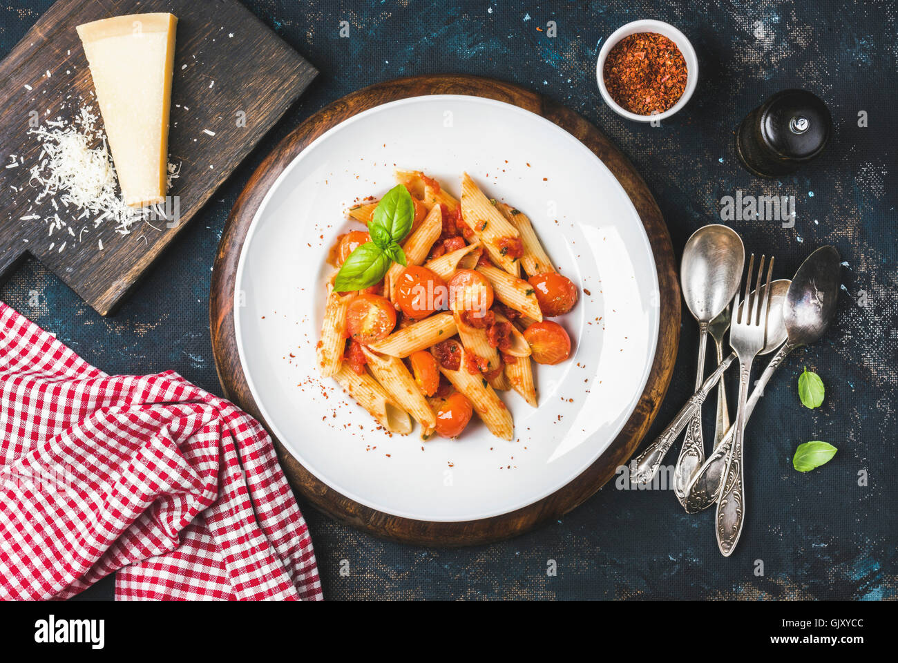 Pasta penne with tomato sauce, basil and roasted tomatoes served with parmesan cheese. Old painted dark plywood background, top Stock Photo