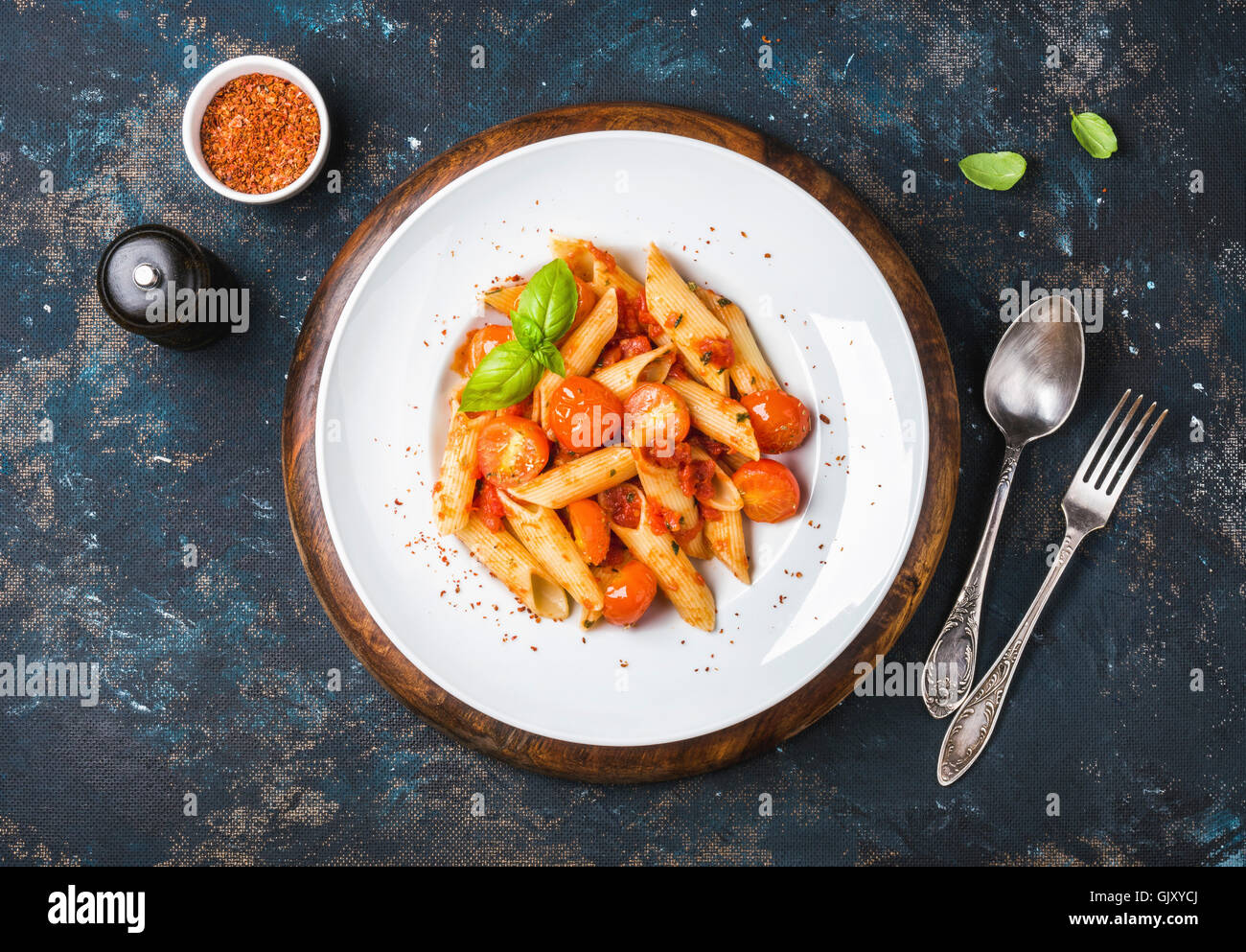 Pasta penne with tomato sauce, fresh basil and roasted tomatoes. Old painted dark plywood background, top view, horizontal compo Stock Photo