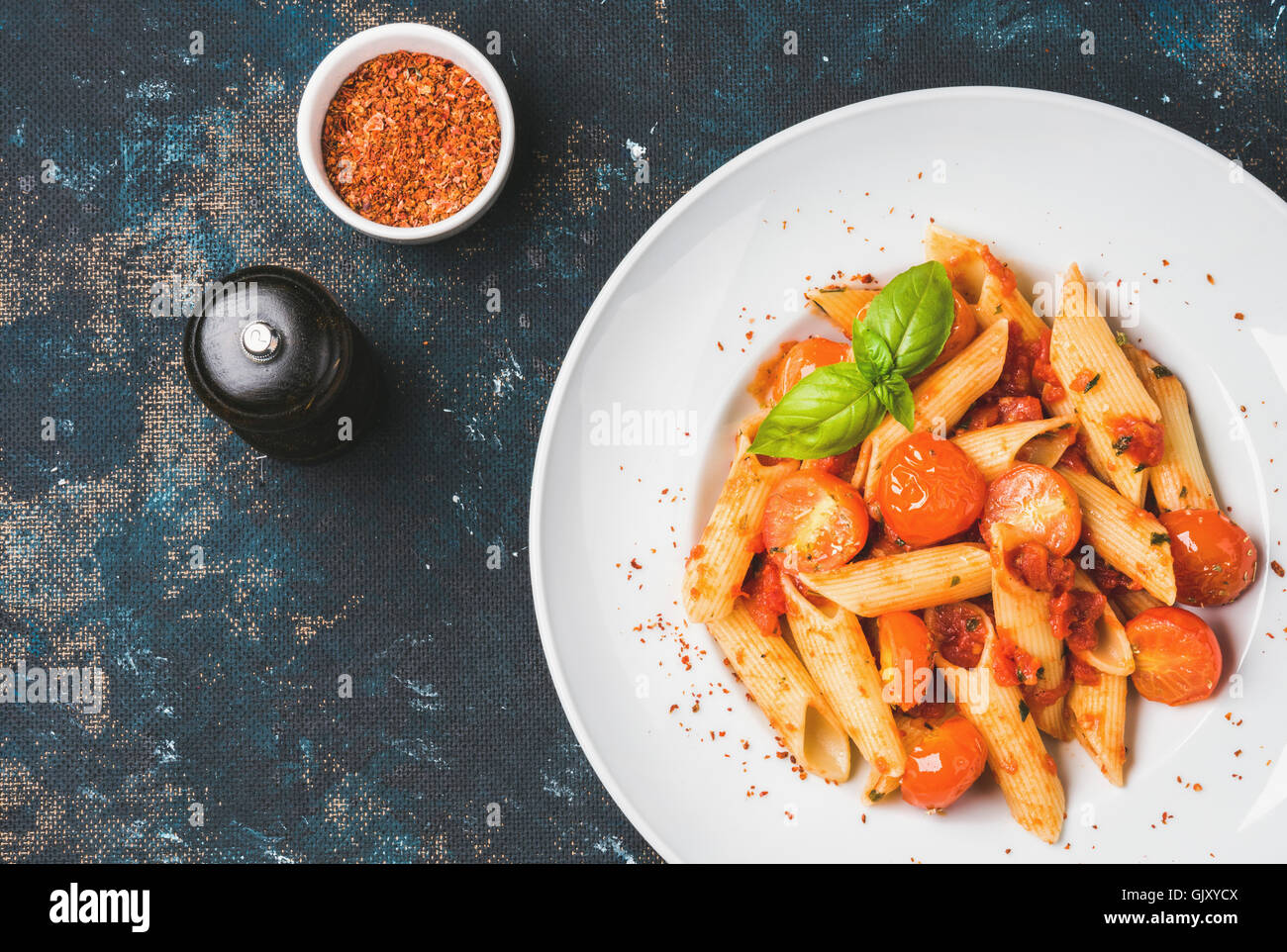 Pasta penne with tomato sauce, basil and roasted tomatoes. Old painted dark plywood background, top view, copy space, horizontal Stock Photo