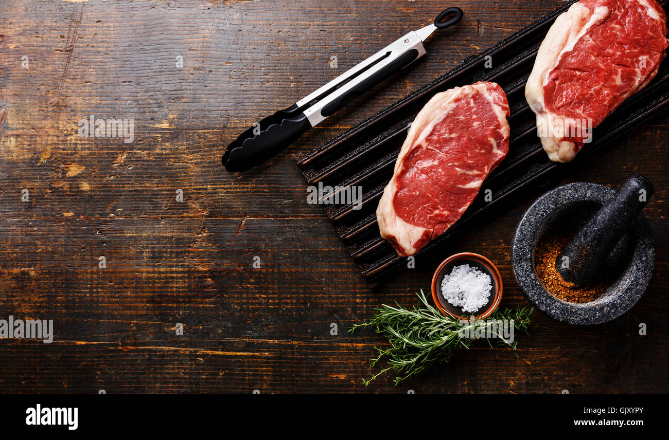 Raw fresh Steak Striploin on black cast iron grill and spices in mortar on wooden background Stock Photo