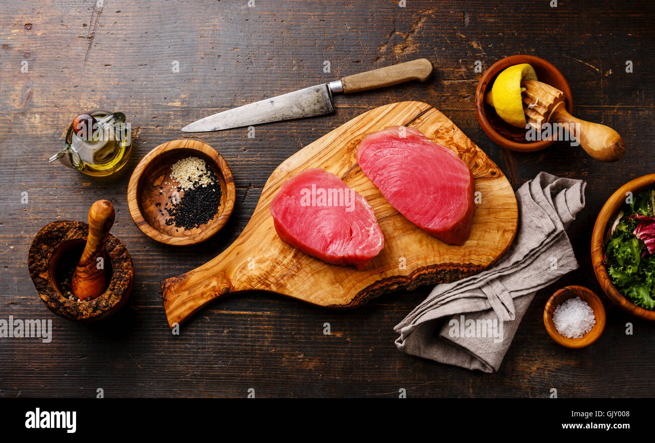 Raw tuna steaks fillet with lemon and sesame on olivewood cutting board on dark wooden background Stock Photo