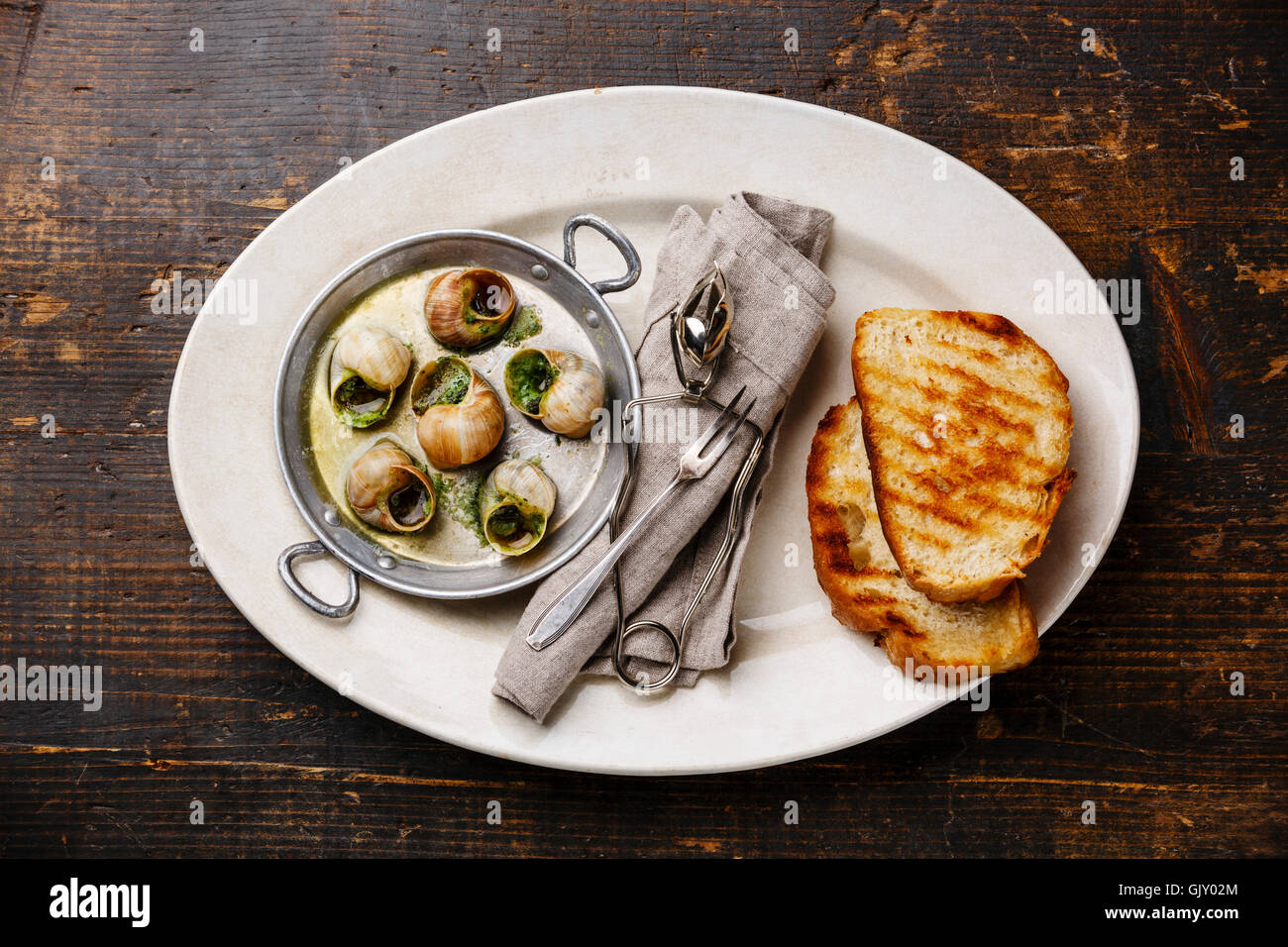 Bourgogne Escargot Snails with garlic herbs butter in aluminum pan and bread toasts on white plate Stock Photo