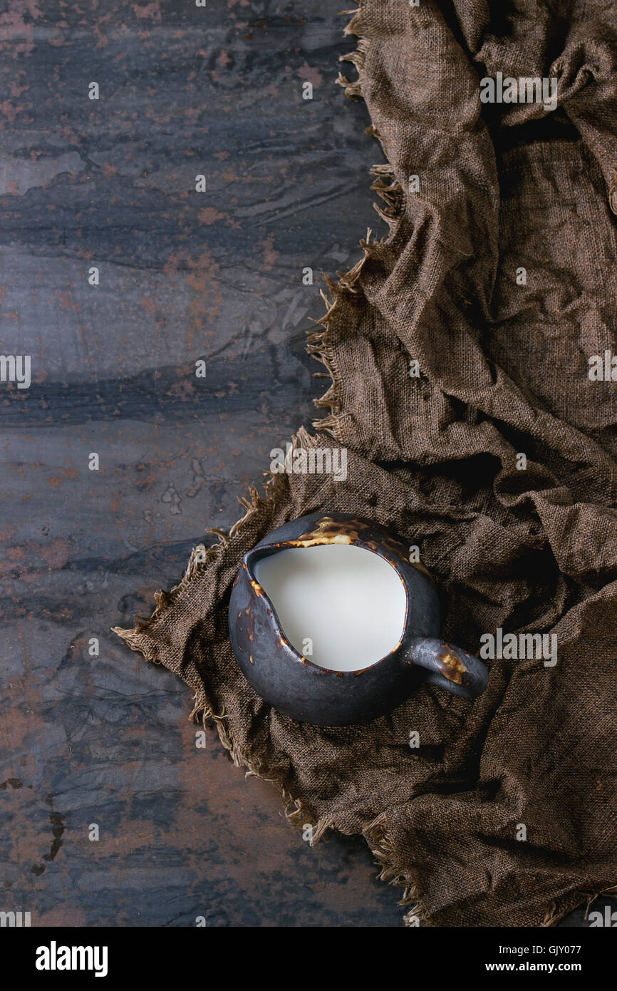 Brown ceramic jug of milk, served on wet sackcloth rag over dark ...