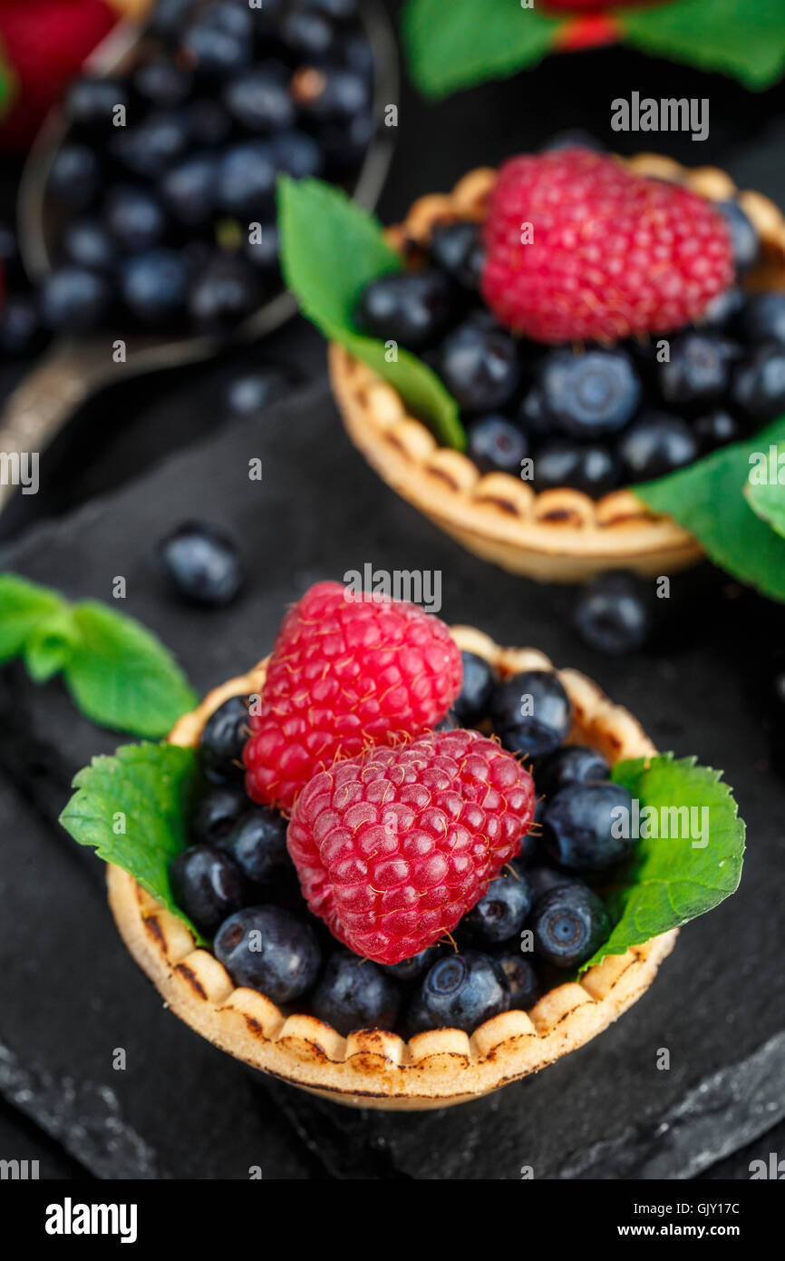 Tartlets with blueberries, raspberries and mint leafs on a black slate background Stock Photo