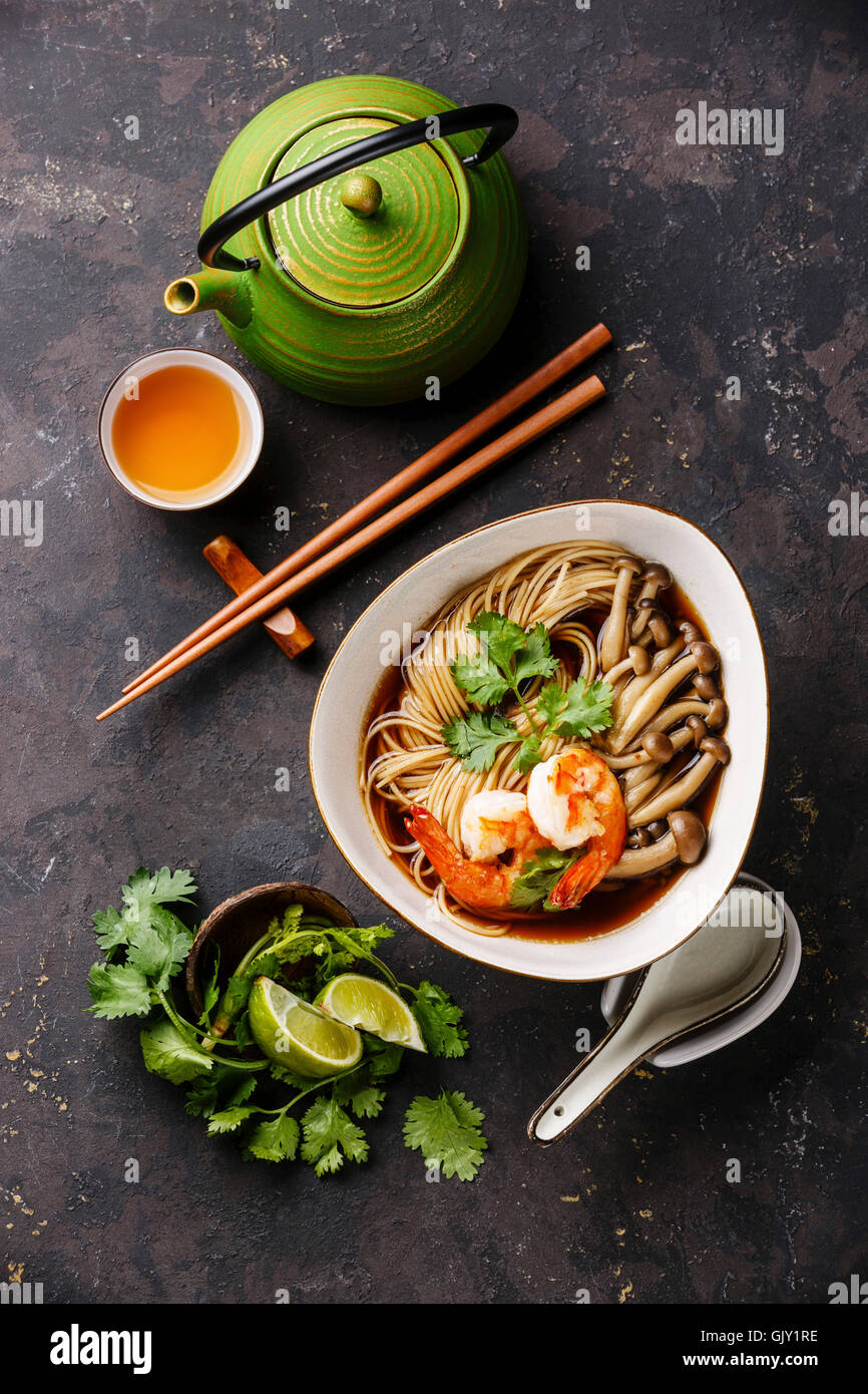Asian Ramen noodles with prawns and shimidzhi mushrooms in broth and Green tea on dark background Stock Photo