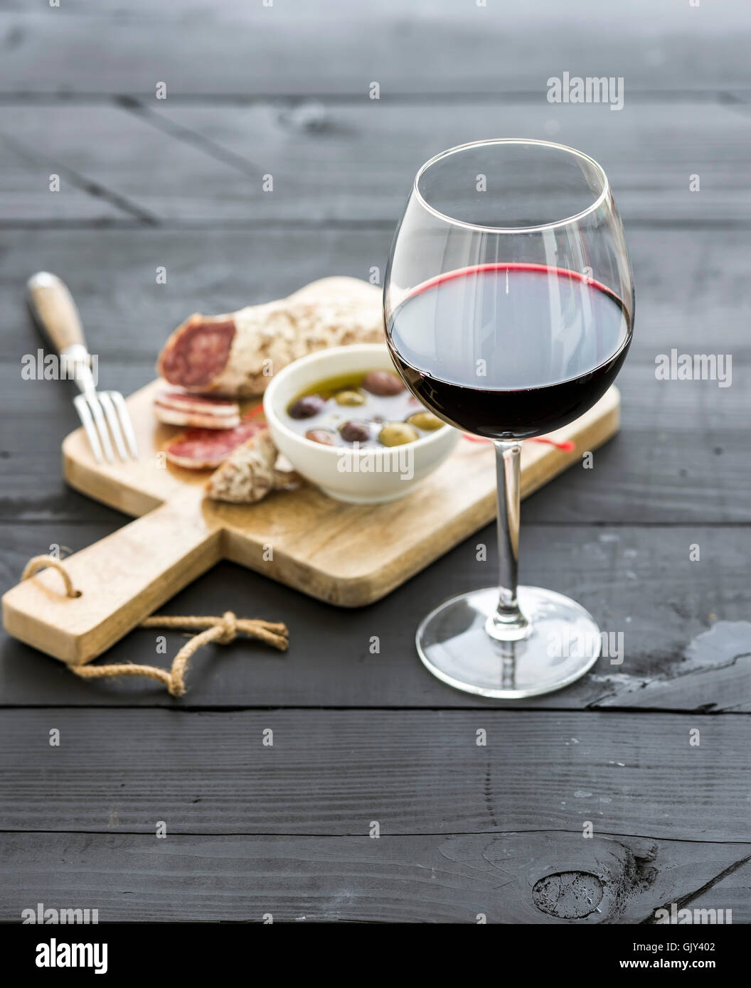 Wine appetizer set. Glass of red wine, French sausage and olives on black wooden backdrop, selective focus, vertical composition Stock Photo