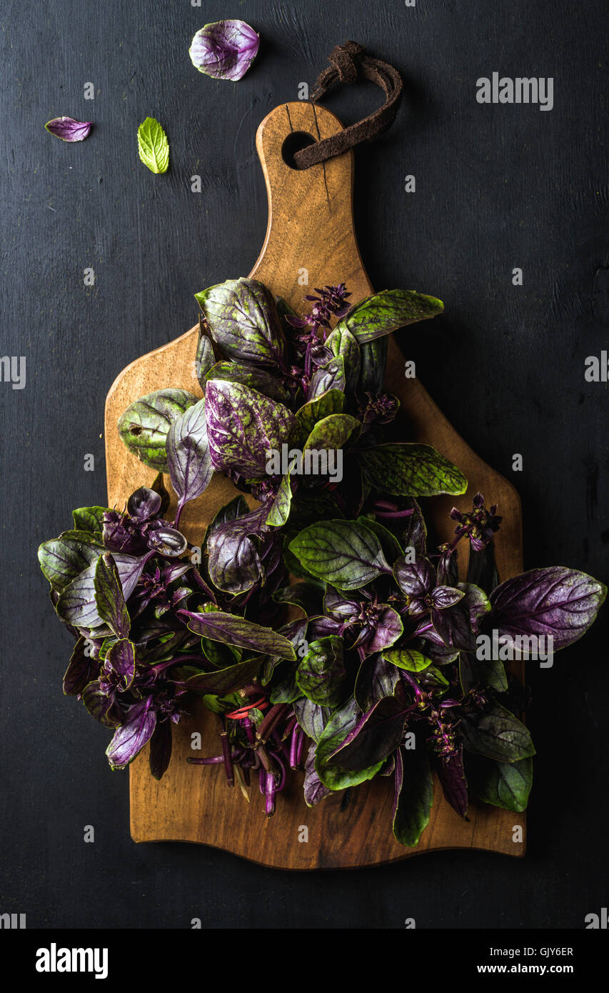 Fresh basil bunches on wooden serving board over dark background, top