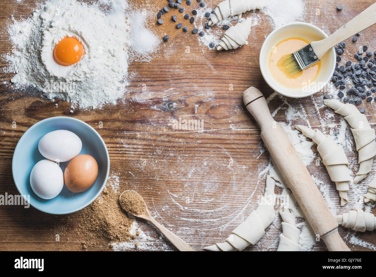 Baking ingredients for cooking croissants. Eggs, brown sugar, melted butter, flour, chocolate chips over rustic wooden backgroun Stock Photo