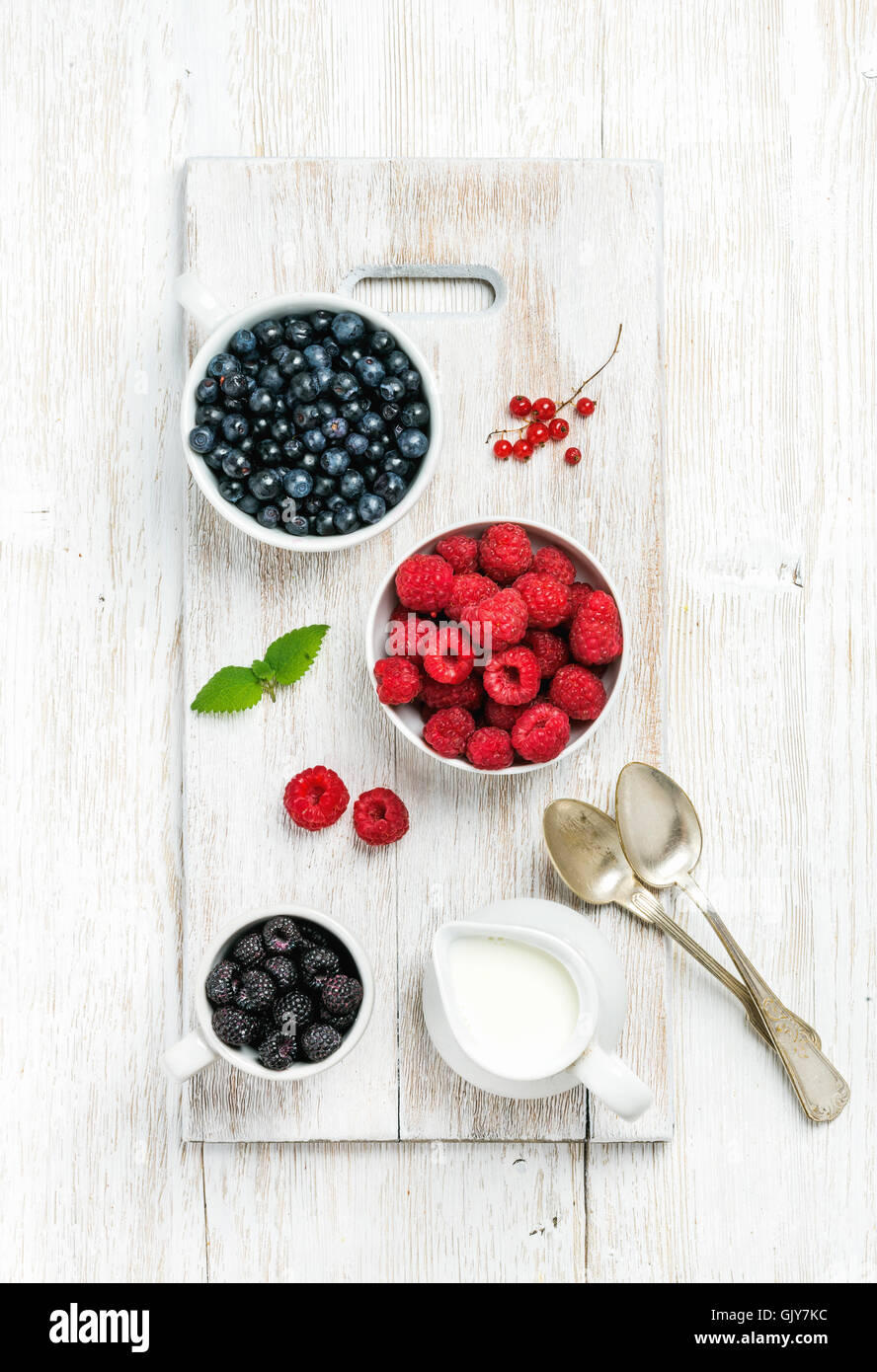 Raspberries, blackberries and bilberries in bowls served with fresh mint, red currant and milk on white painted wooden backgroun Stock Photo