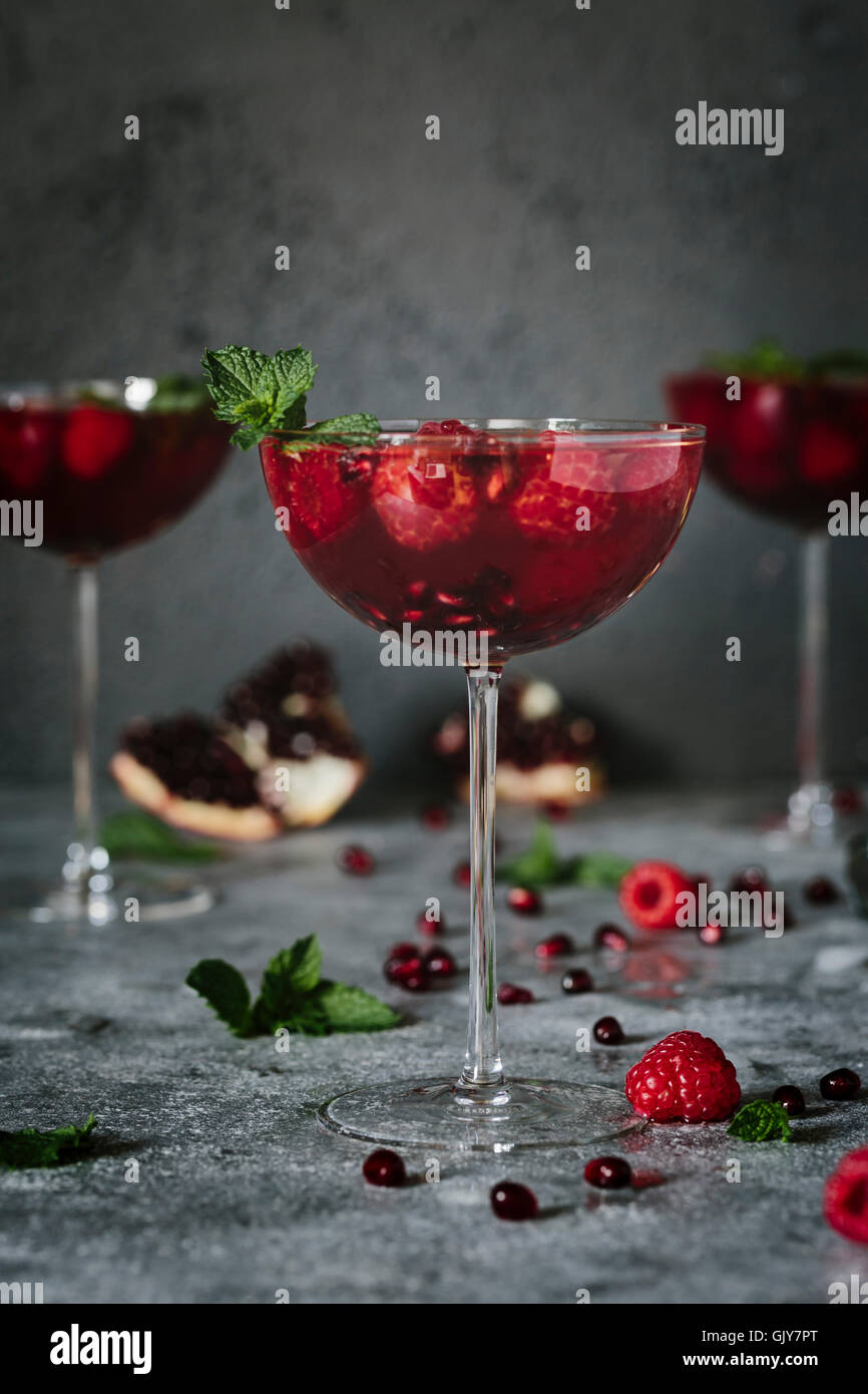 A coupe glass of Raspberry and Pomegranate Champagne Cocktailed garnished with mint is photographed (with 2 other out of focus) Stock Photo