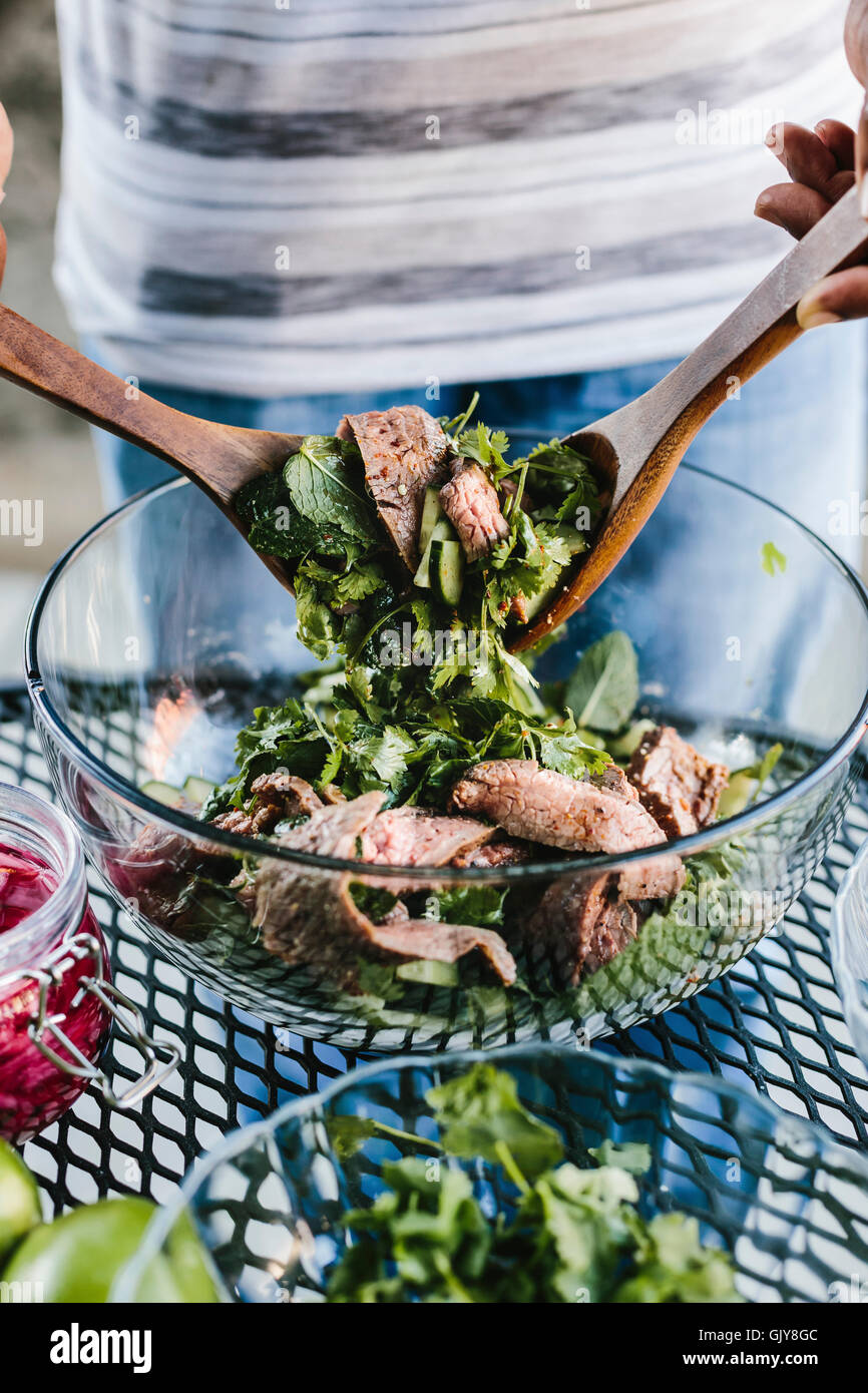 A man is mixing grilled steak with fresh herbs. Stock Photo