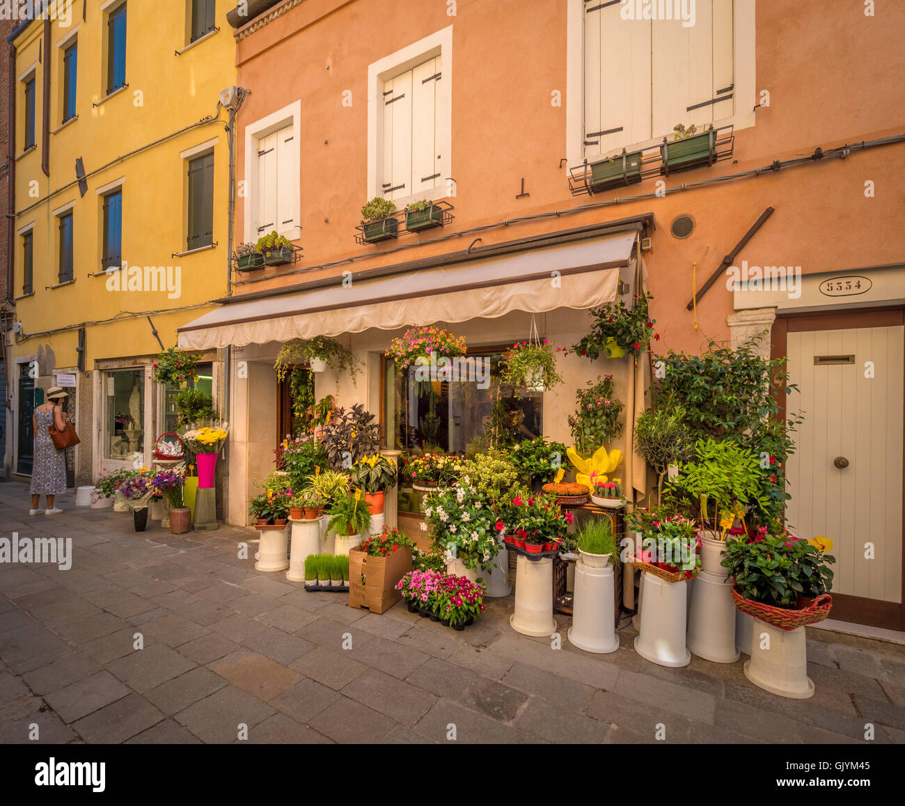 Venetian flower shop in a residential square or campo. Mature female looking in the window. Venice, italy. Stock Photo