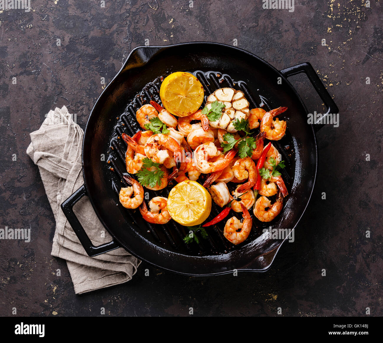 Prawns roasted on frying grill pan with lemon and garlic on dark background Stock Photo