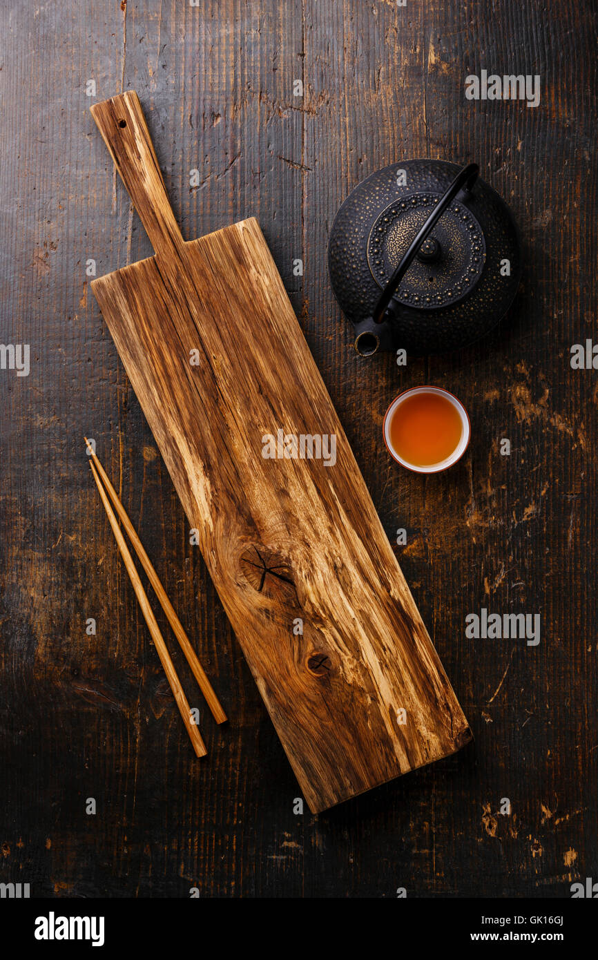 Wooden serving board for Sushi, chopsticks and green tea in teapot on wooden background Stock Photo
