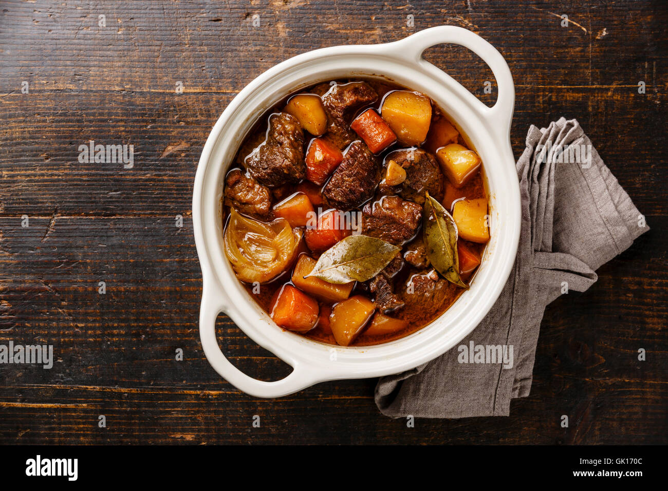 Beef meat stewed with potatoes, carrots and spices in ceramic pot on wooden background Stock Photo