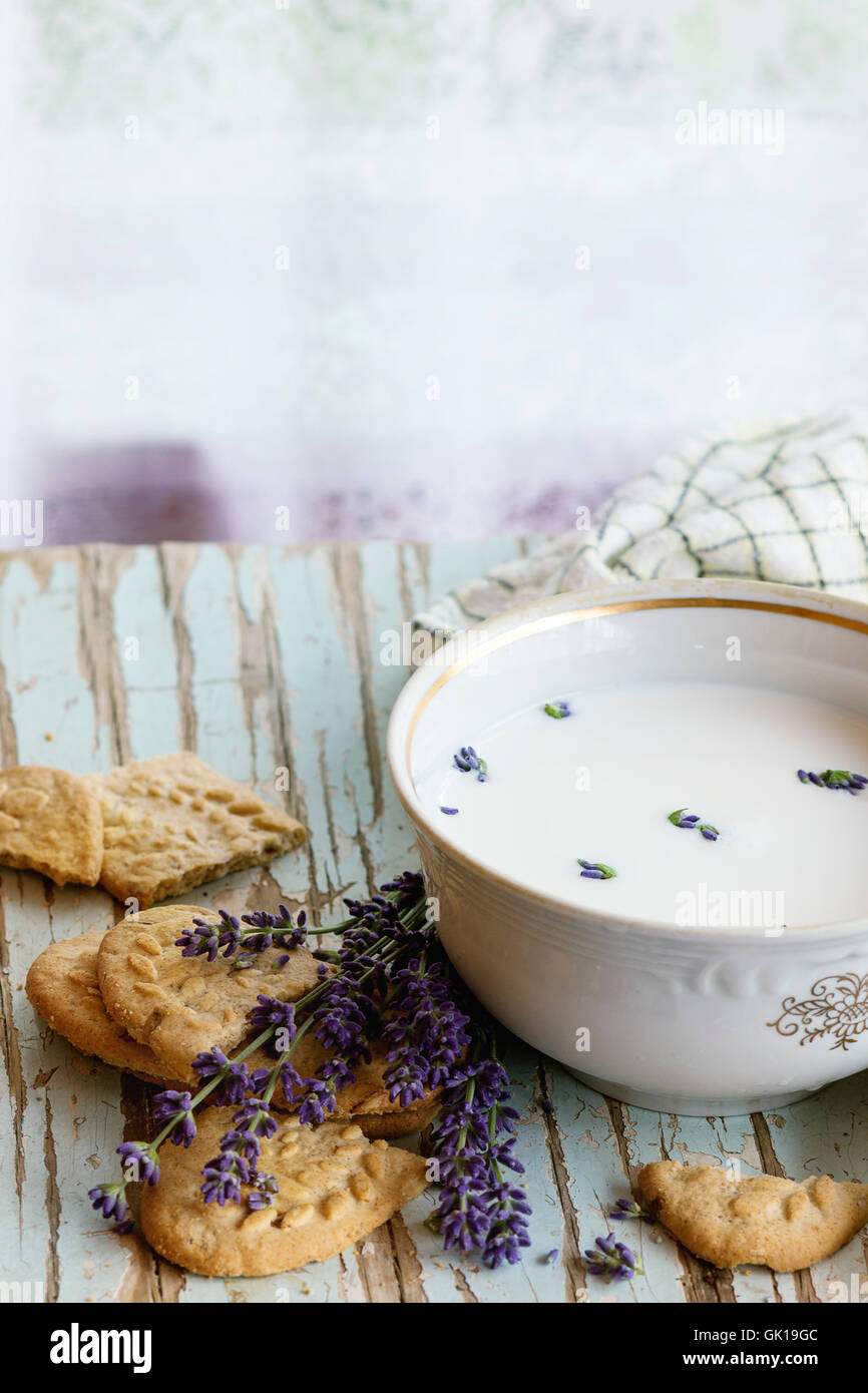 Lavender cookies and bowl of aromatic milk, served with kitchen towel on old wooden table with window at background. Breakfast i Stock Photo