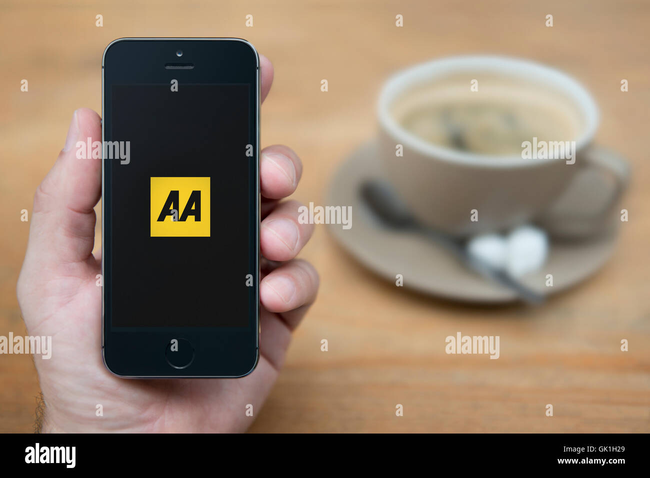 A man looks at his iPhone which displays the AA logo, while sat with a cup of coffee (Editorial use only). Stock Photo