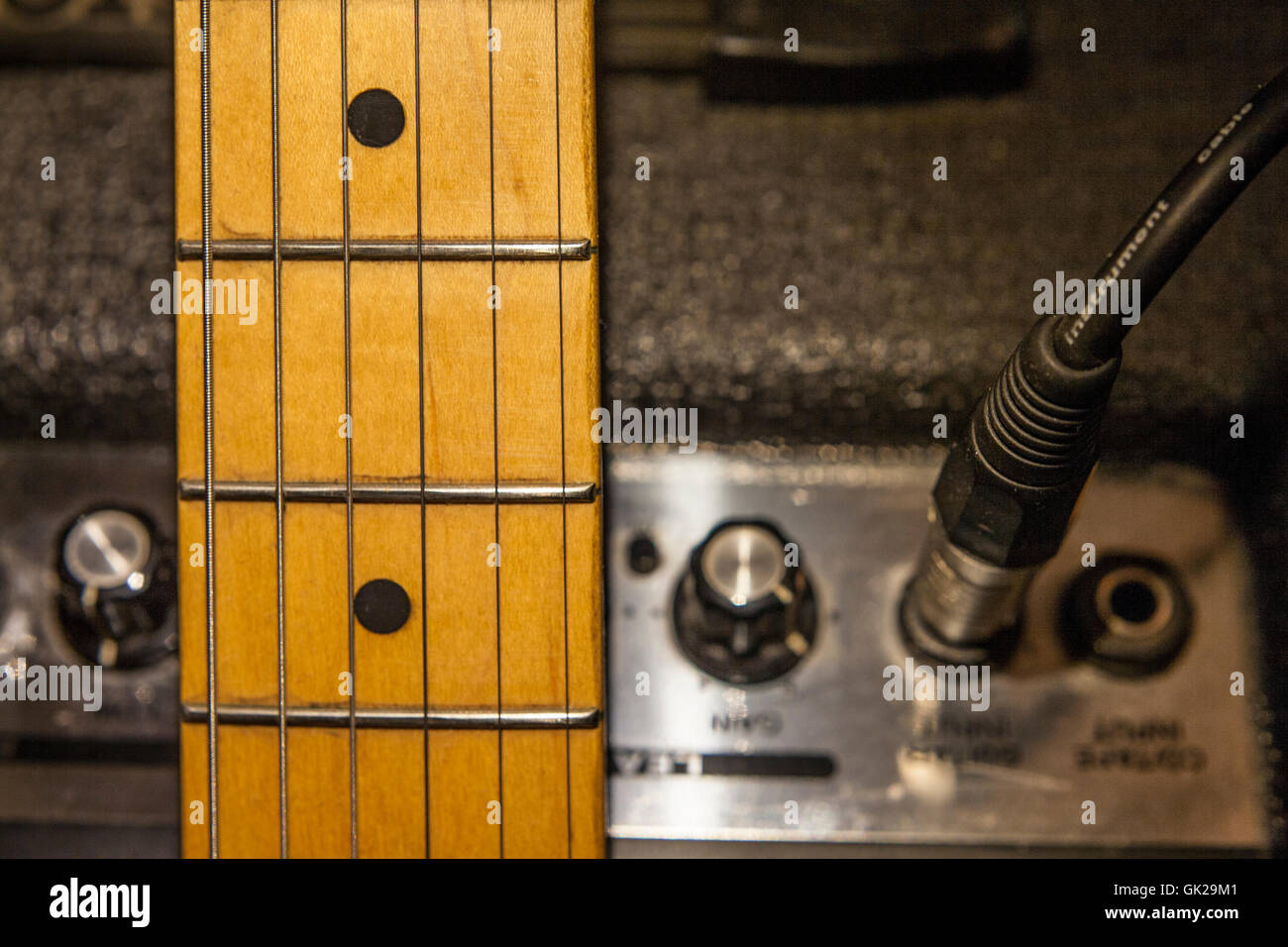 Guitar neck over amplifier device and audio cord with jack closeup Stock Photo