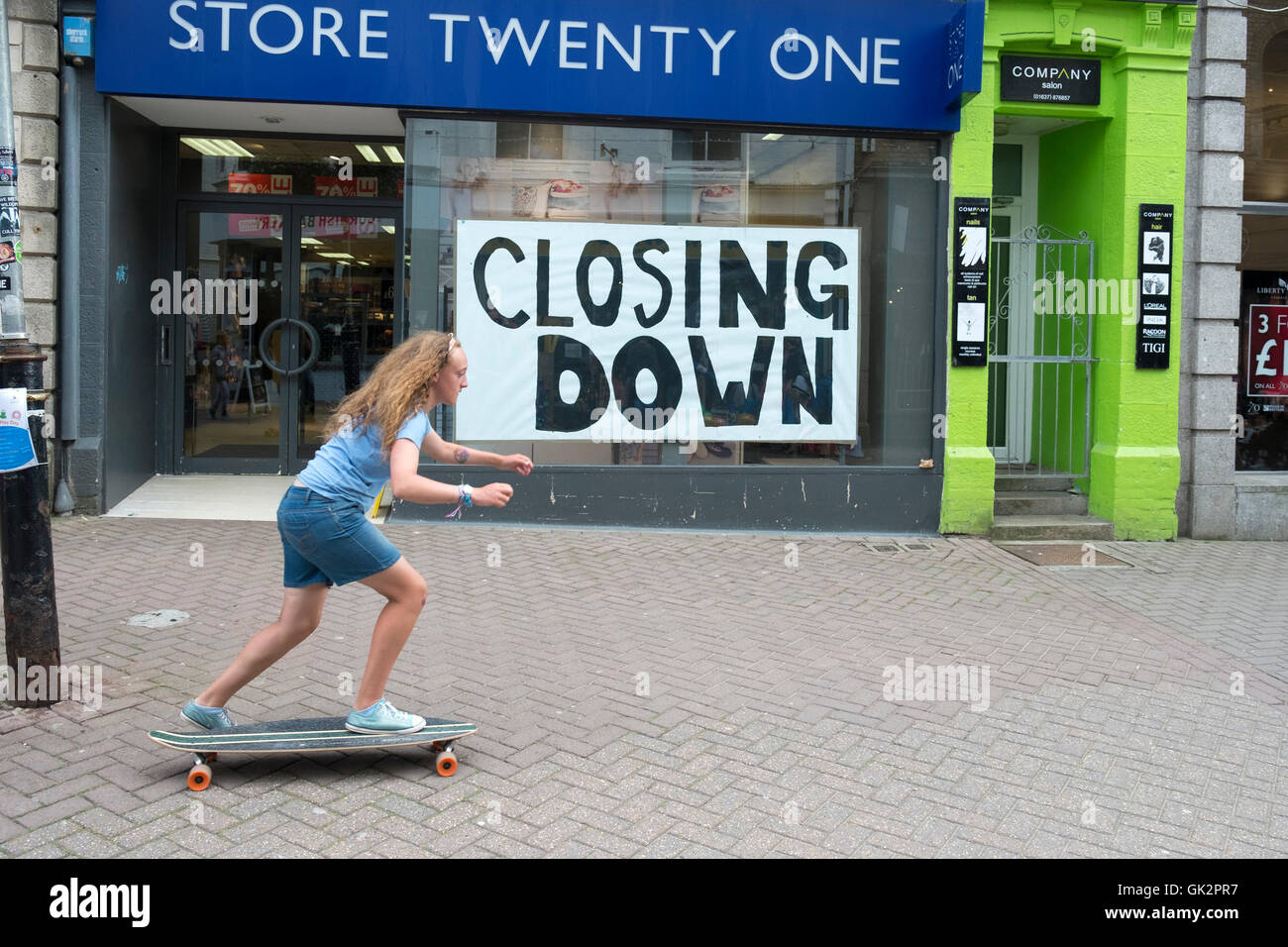 A young girl skateboarding past a shop that is closing down in Newquay, Cornwall. Stock Photo