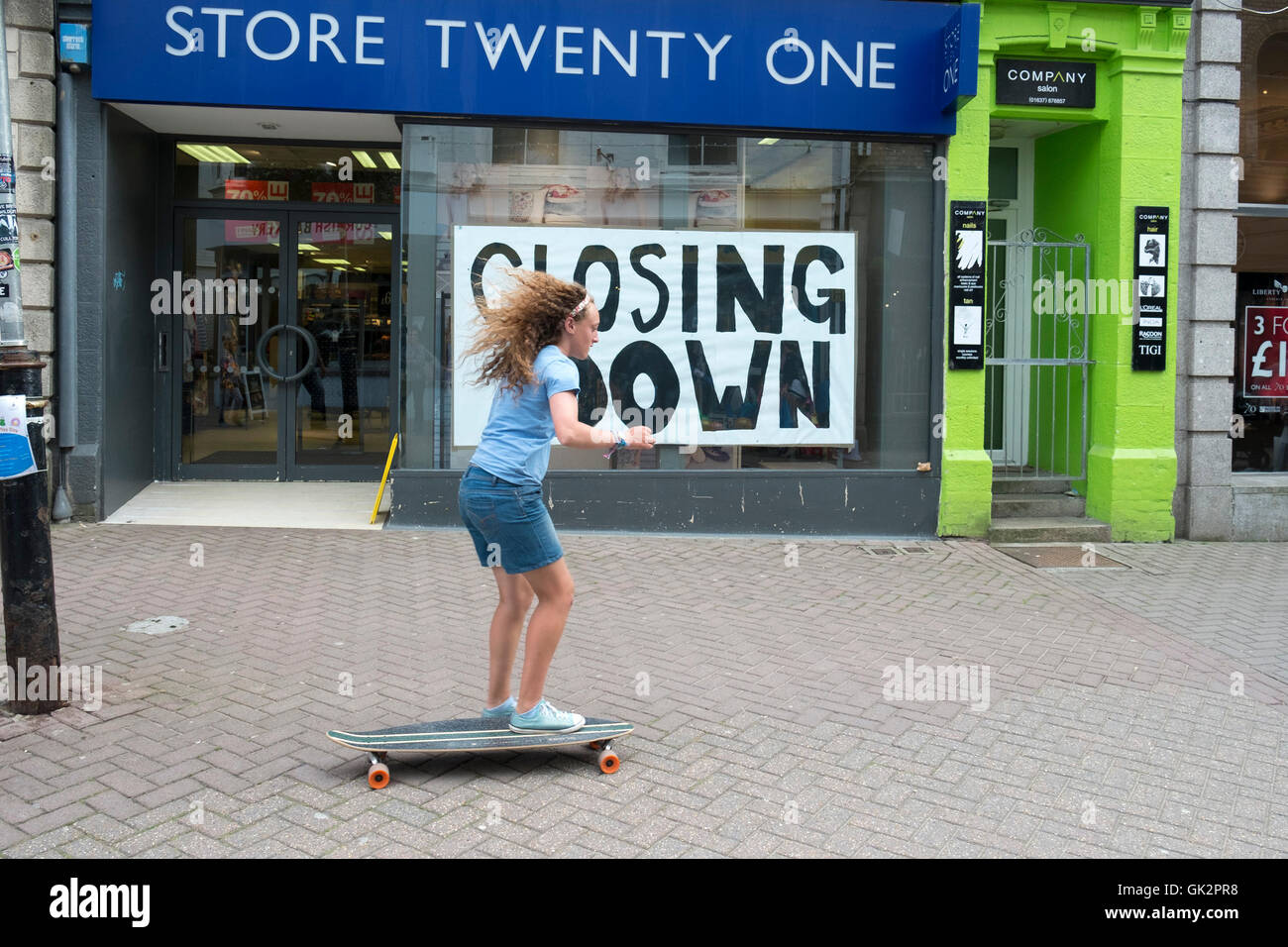 A young girl skateboarding past a shop that is closing down in Newquay Town Centre, Cornwall, England, UK. Stock Photo