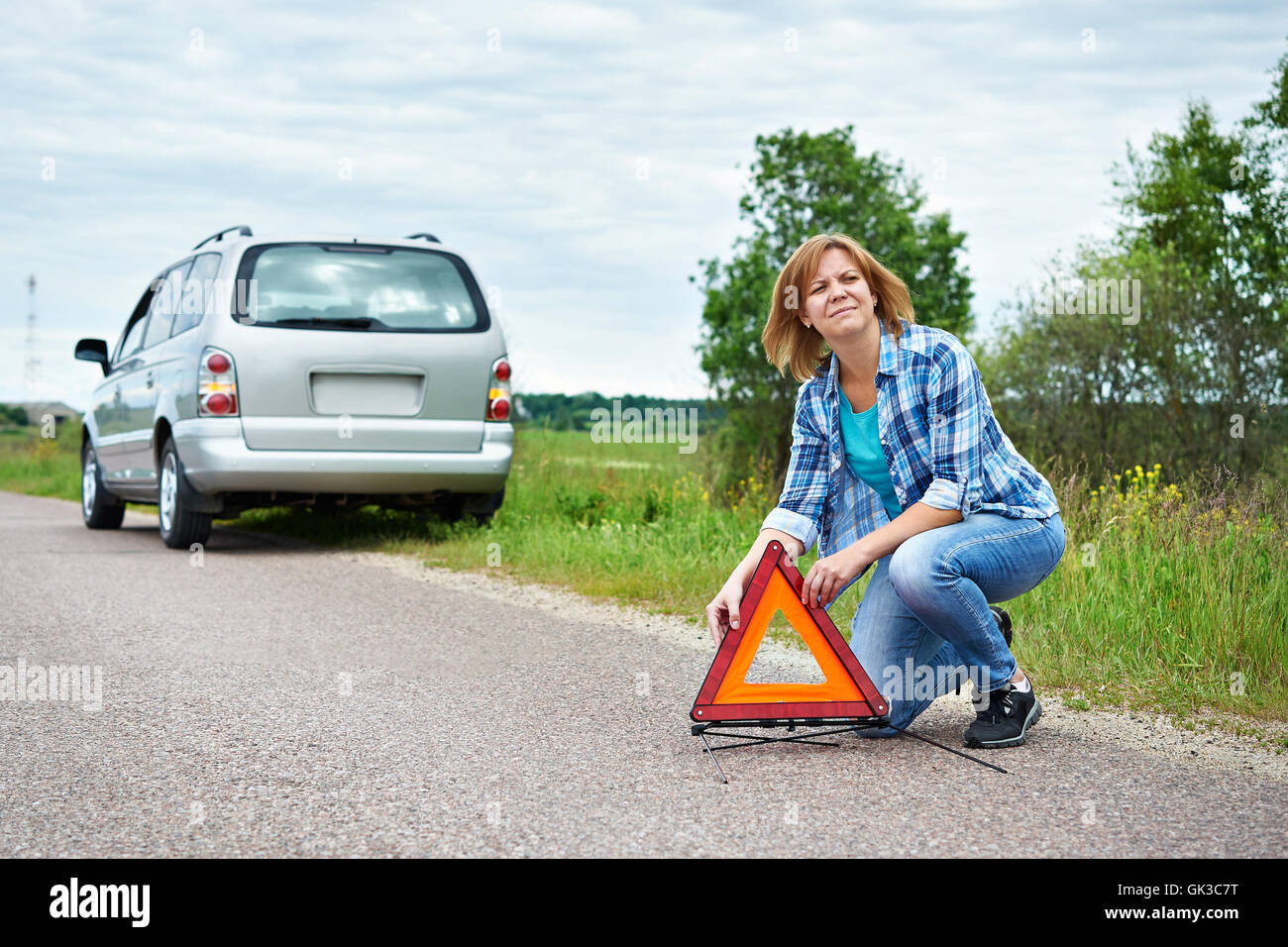 Woman installing emergency sign on road near broken car Stock Photo