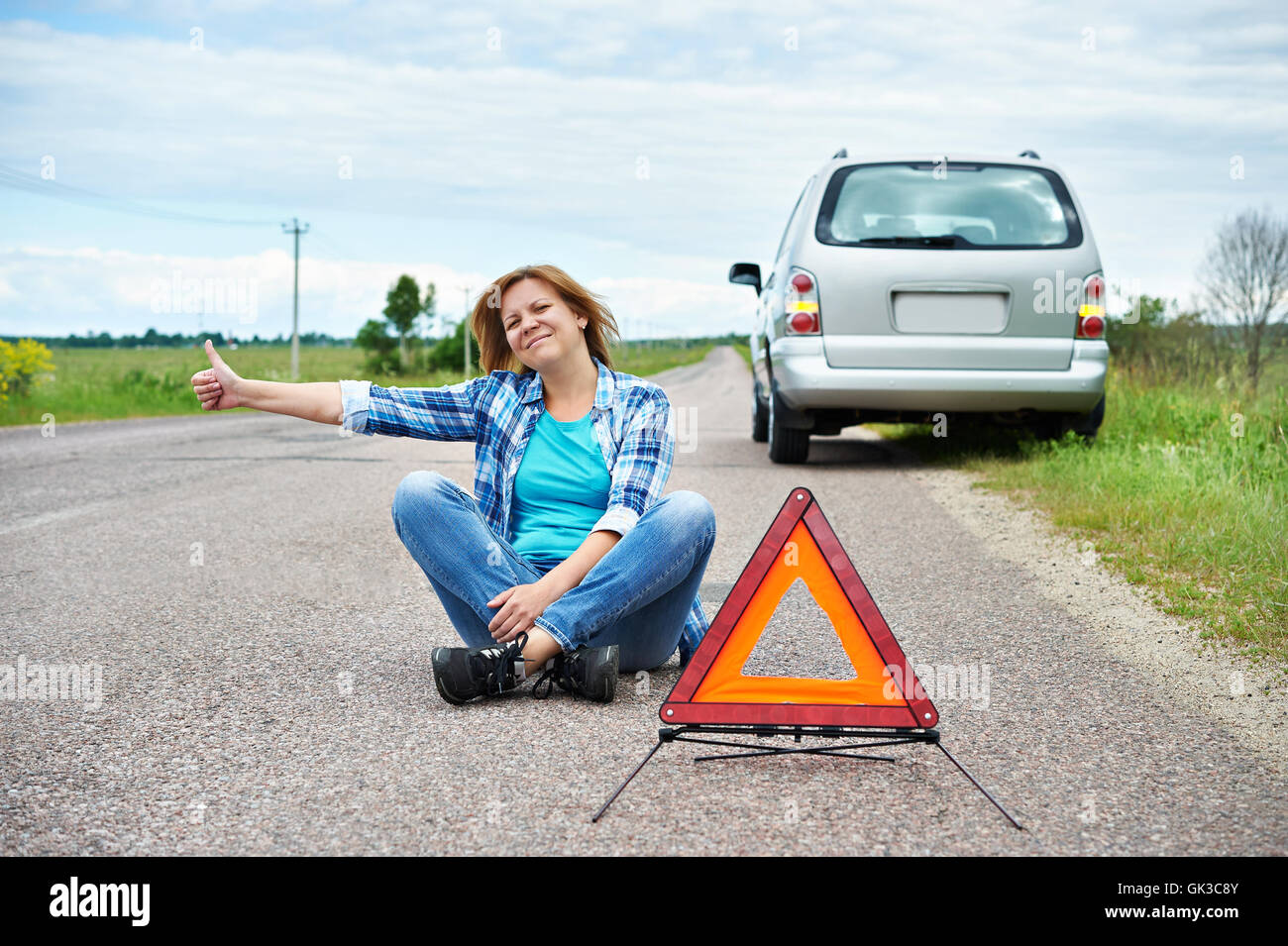 Woman sitting on road near emergency sign and showing thumbs up Stock Photo
