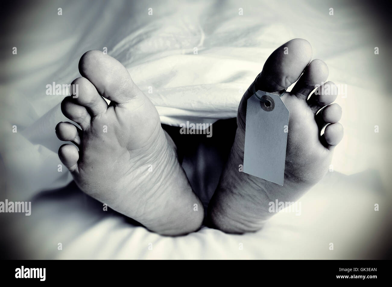closeup of the feet of a dead body covered with a sheet, with a blank tag tied on the big toe of his left foot, in monochrome, w Stock Photo