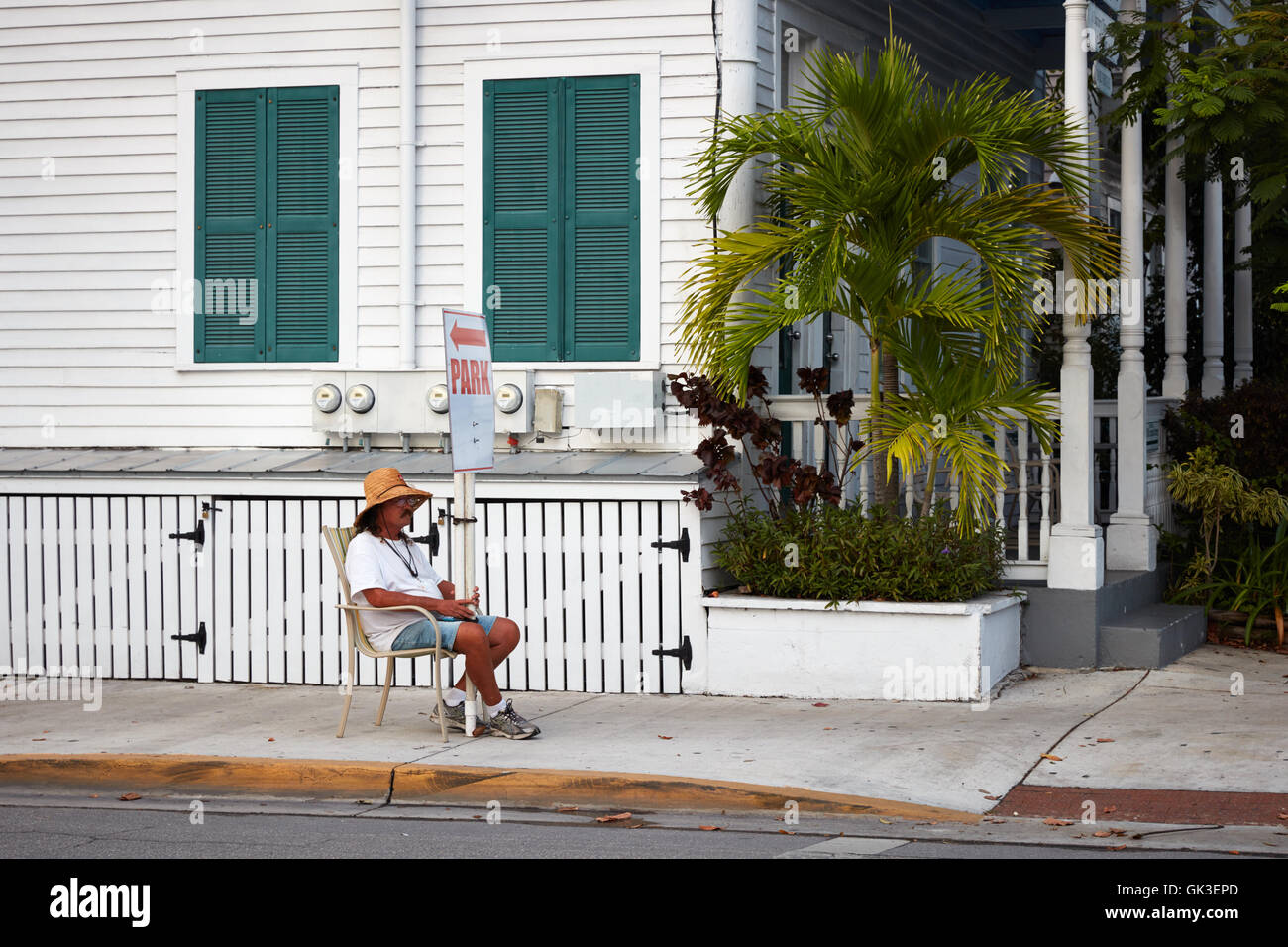 Man sitting in a chair holding a direction sign for parking in Key West