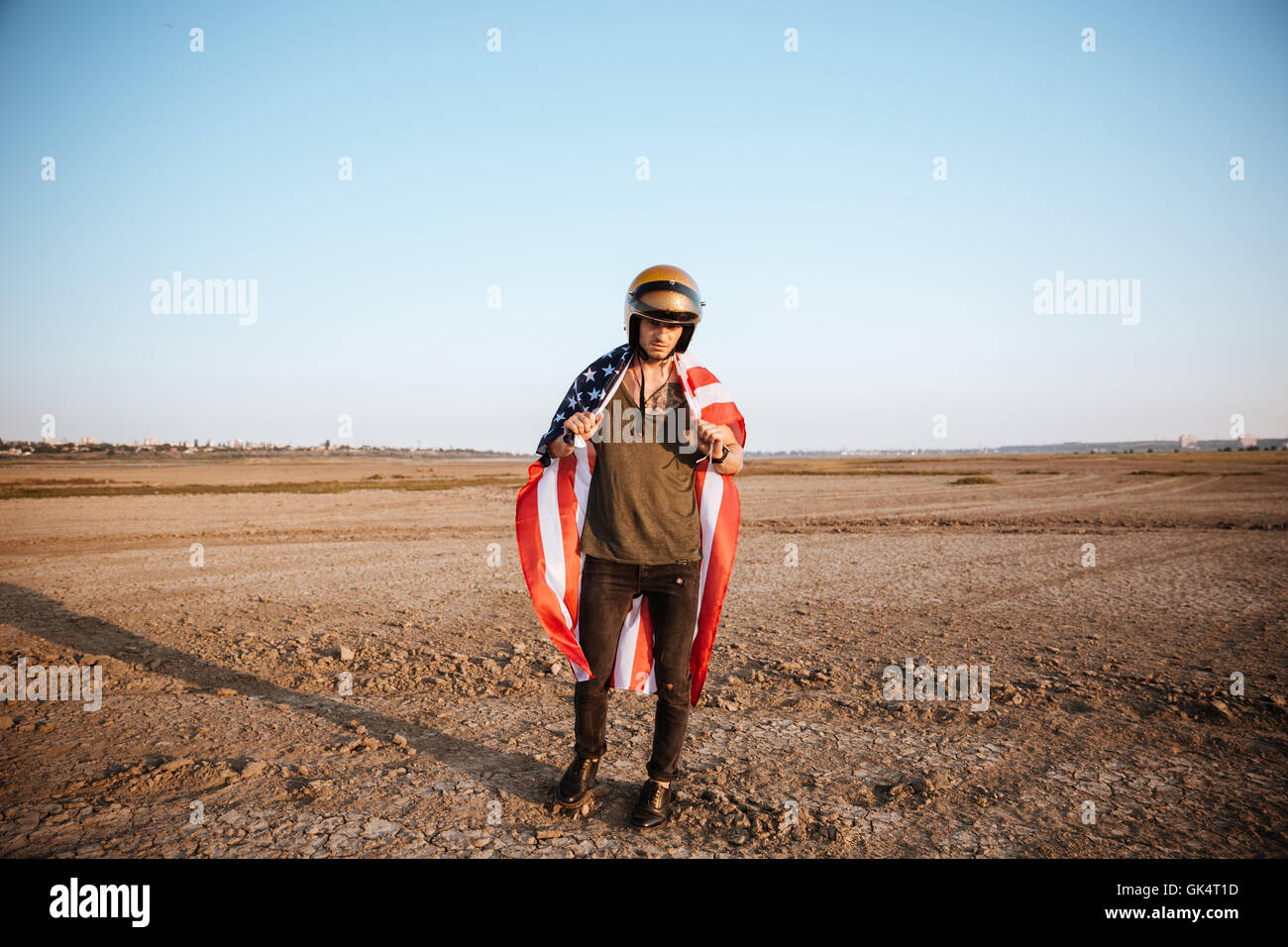 Young brutal man wearing american flag cape and golden helmet posing at
