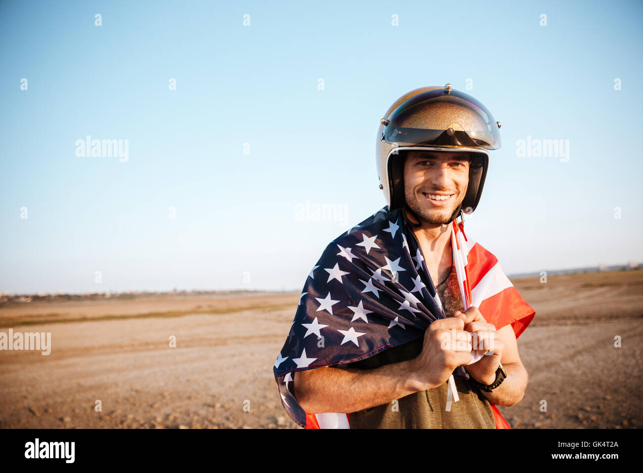 Young smiling brutal man wearing american flag cape and golden looking