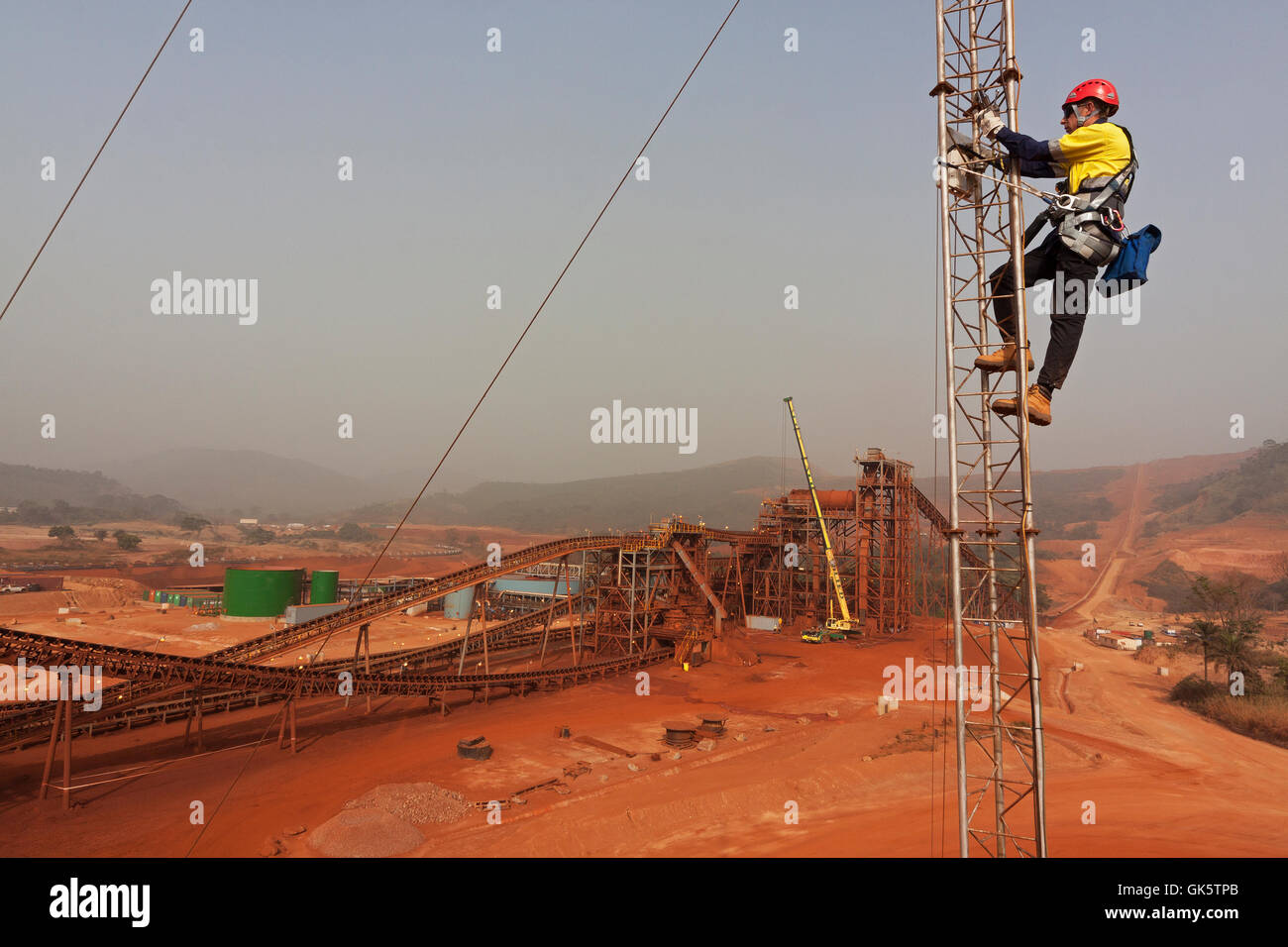 Iron ore mine in Sierra Leone towards process plant.Telecoms engineer up tower working on microwave radio network link, adjusting antenna alignment. Stock Photo