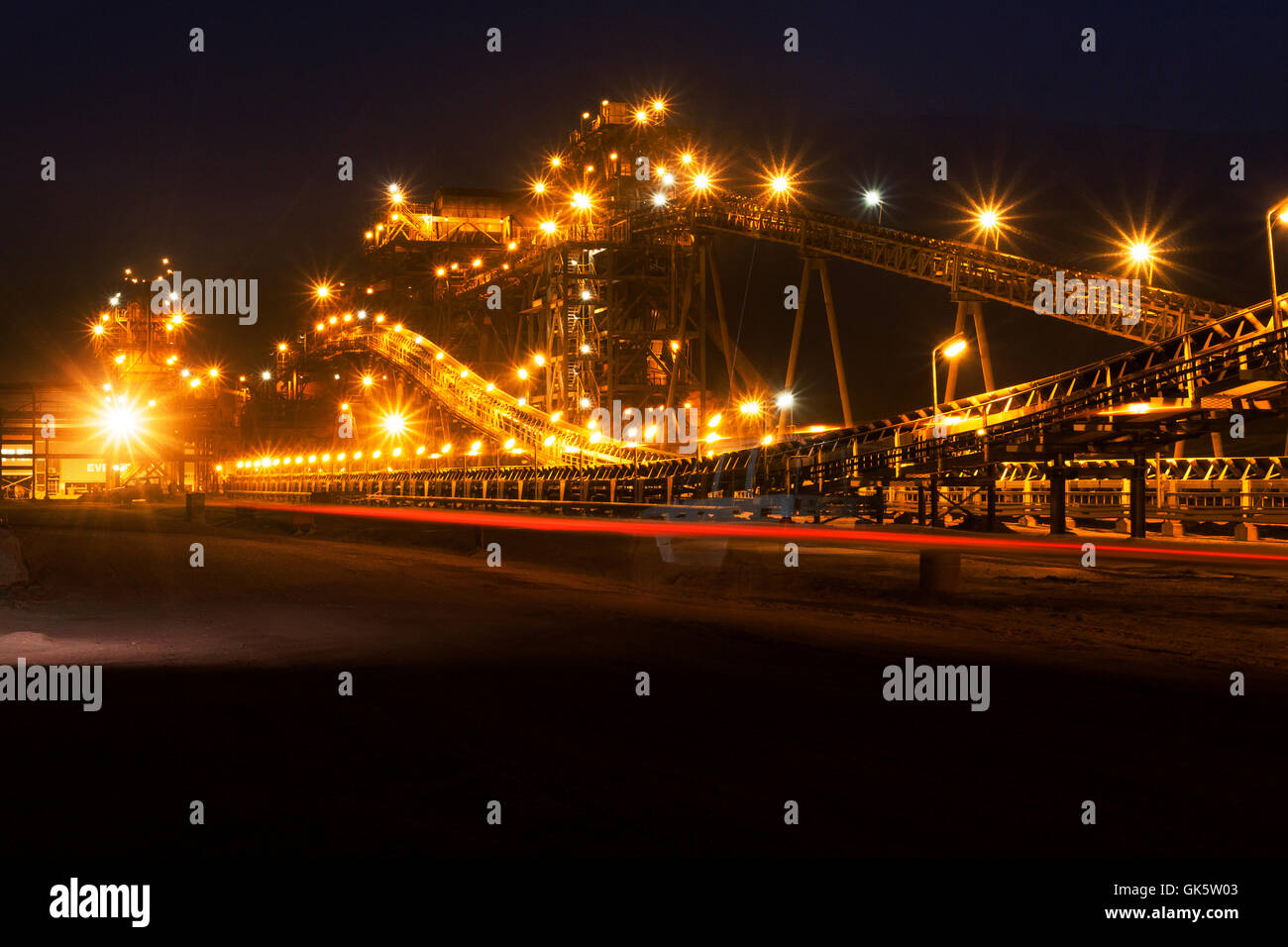 Mining operations for transporting and managing iron ore. Night view of new mine processing plant lit up and illuminated by car lights. West Africa. Stock Photo