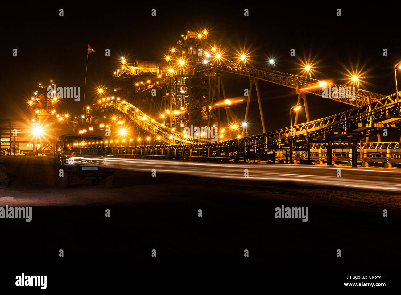 Mining operations for transporting and managing iron ore. Night view of new processing plant lit up and illuminated by truck headlights. West Africa. Stock Photo