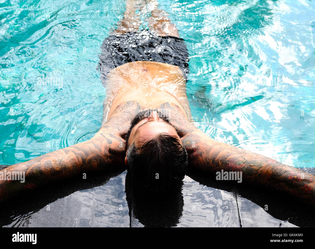 A man with tattoos resting on the side of a pool in Bali Stock Photo