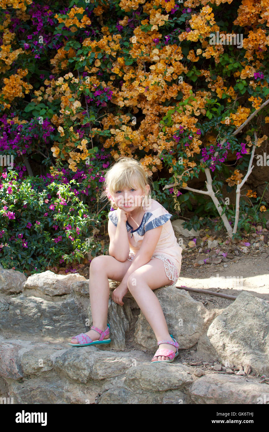 young girl sitting in front of wall of flowers at park guell Stock Photo