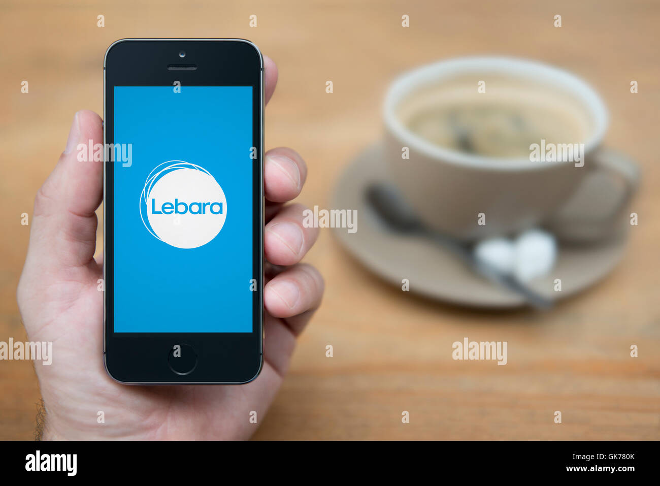 A man looks at his iPhone which displays the Lebara Mobile logo, while sat with a cup of coffee (Editorial use only). Stock Photo