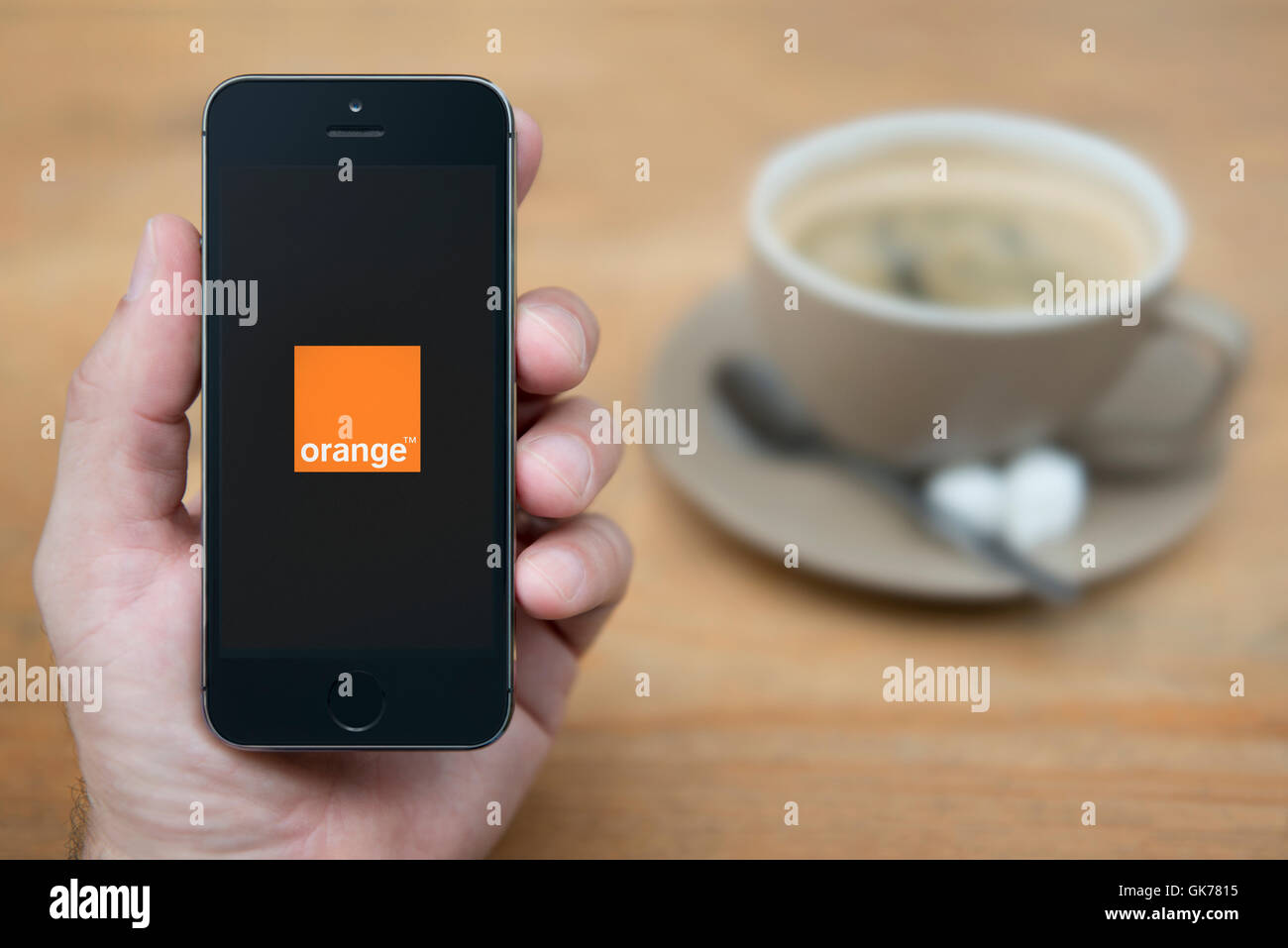 A man looks at his iPhone which displays the Orange logo, while sat with a cup of coffee (Editorial use only). Stock Photo