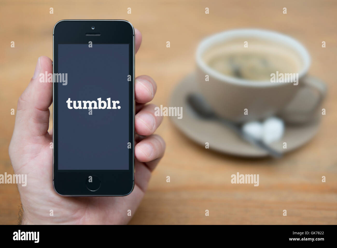 A man looks at his iPhone which displays the Tumblr logo, while sat with a cup of coffee (Editorial use only). Stock Photo