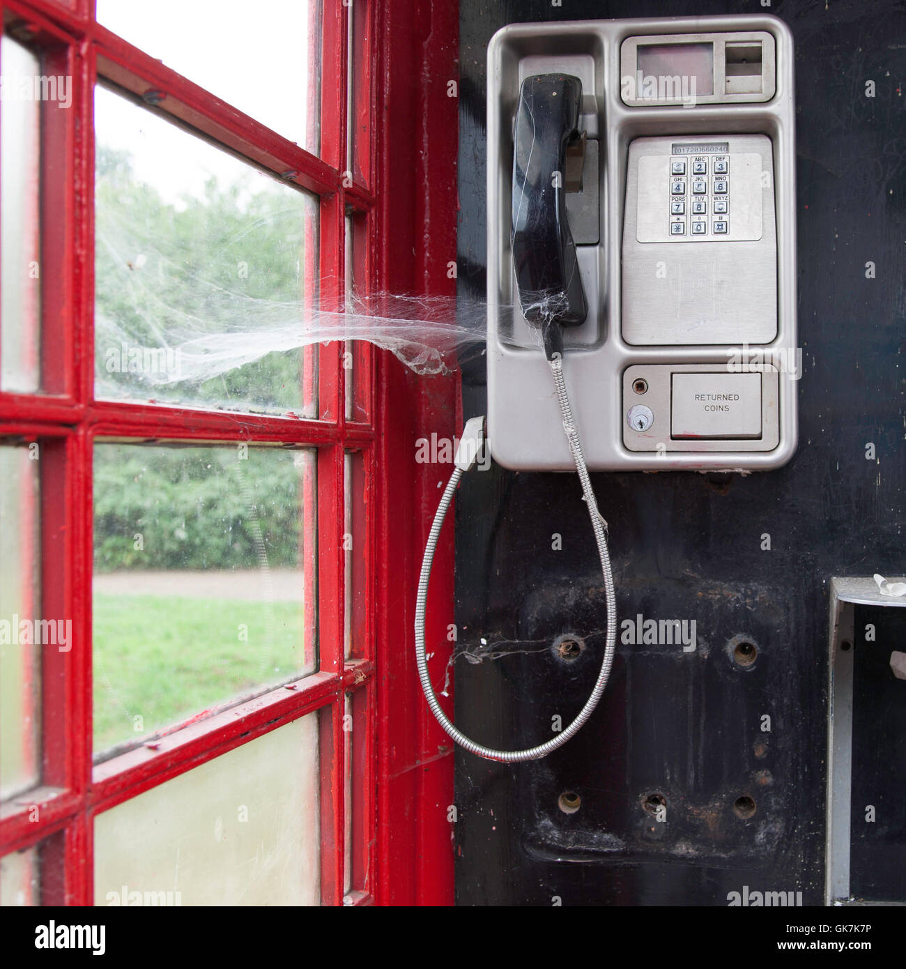 A traditional red public telephone box in a rural setting in the United Kingdom shows a spider's web over the handset. Symbol of obsolescence. Rarely used telephone box with cobwebs in Waveney, England Stock Photo