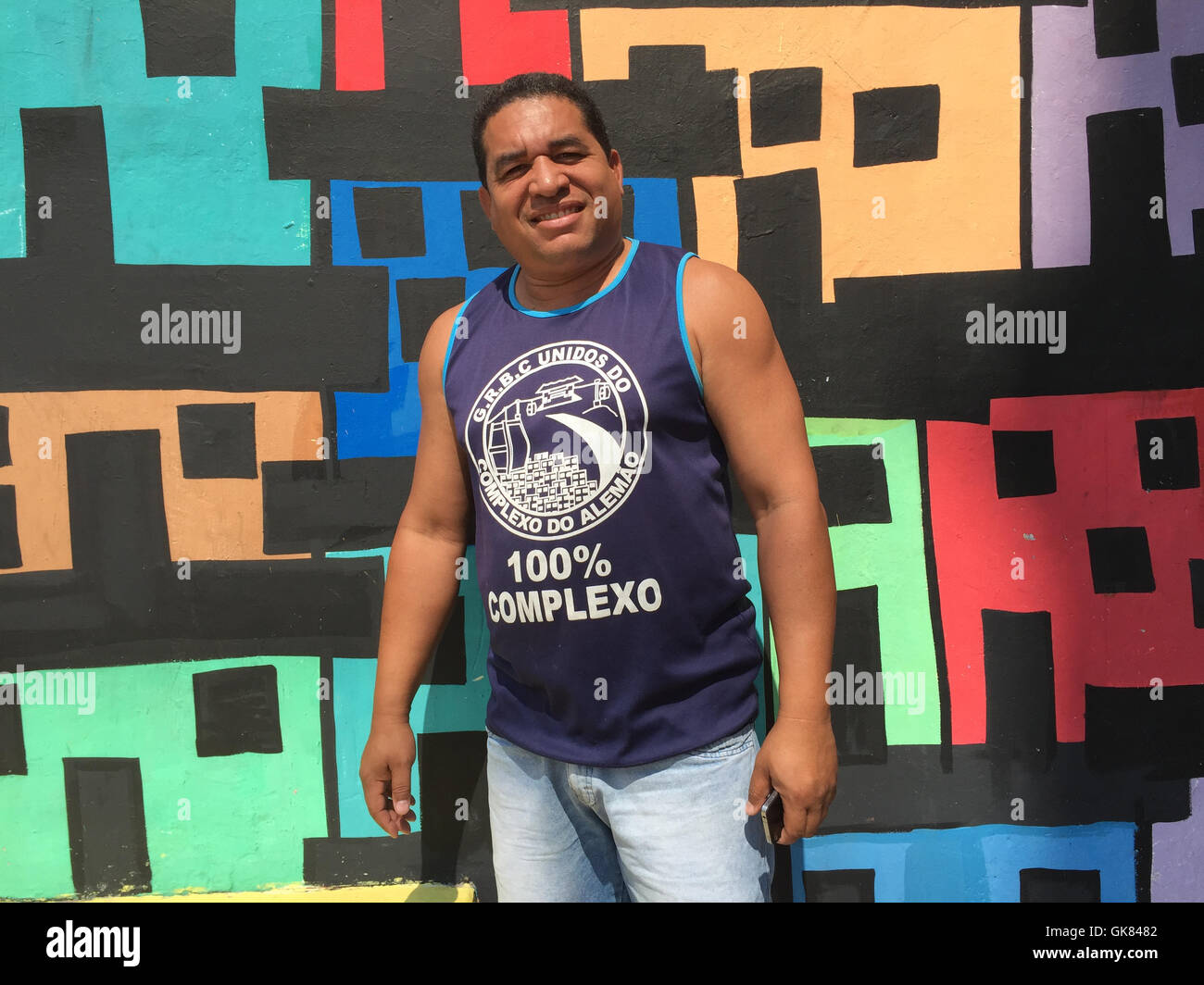 Rio de Janeiro, Brazil. 18th Aug, 2016. Cleber Araujo pictured in front of a colourfully-painted wall, with which he and his wife want to take a stand against violence and illustrate the colourful life here, in the Complexo do Alemao favela, in Rio de Janeiro, Brazil, 18 August 2016. In 2014, there were more than 50 deaths here as the result of violent clashes. PHOTO: GEORG ISMAR/dpa/Alamy Live News Stock Photo