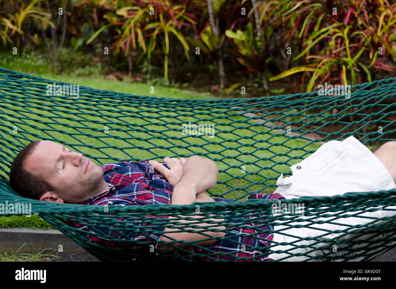 Man sleeping in a hammock with his arms crossed and eyes closed. Stock Photo