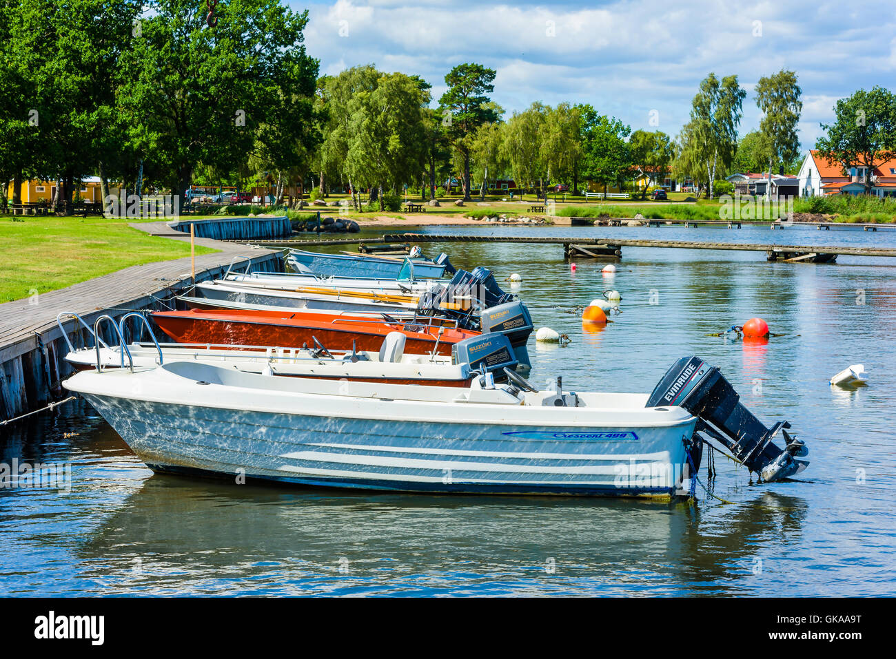 Hagby, Sweden - August 10, 2016: Some small boats moored dockside at a vocational village with public park in the background. Stock Photo